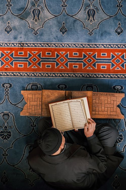 Free Overhead view of a man reading religious texts in a mosque with intricate carpet design. Stock Photo