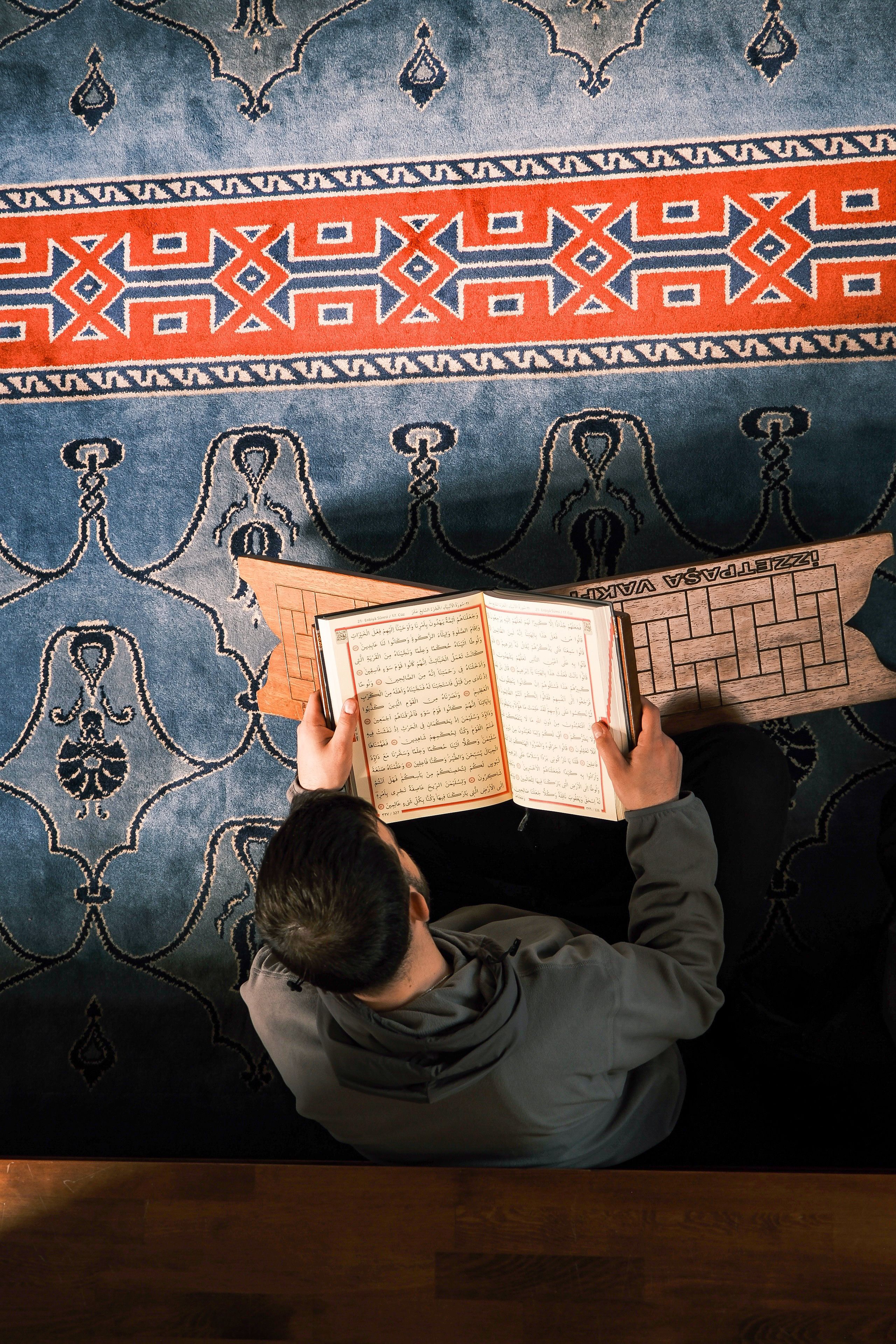 Person Reading Religious Text on Ornate Carpet · Free Stock Photo