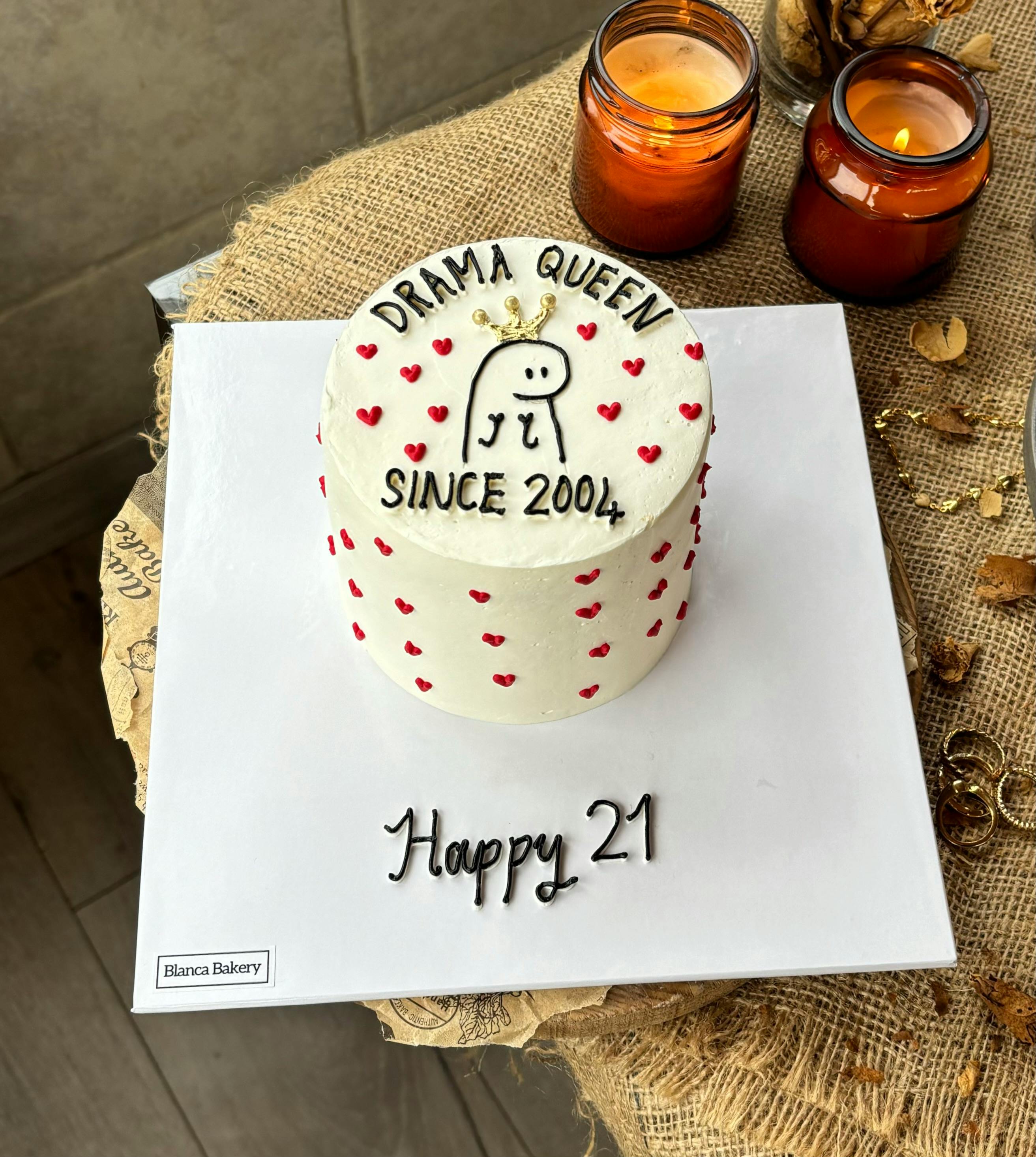 White cake with "Drama Queen Since 2004" design celebrating a 21st birthday, decoratively styled.