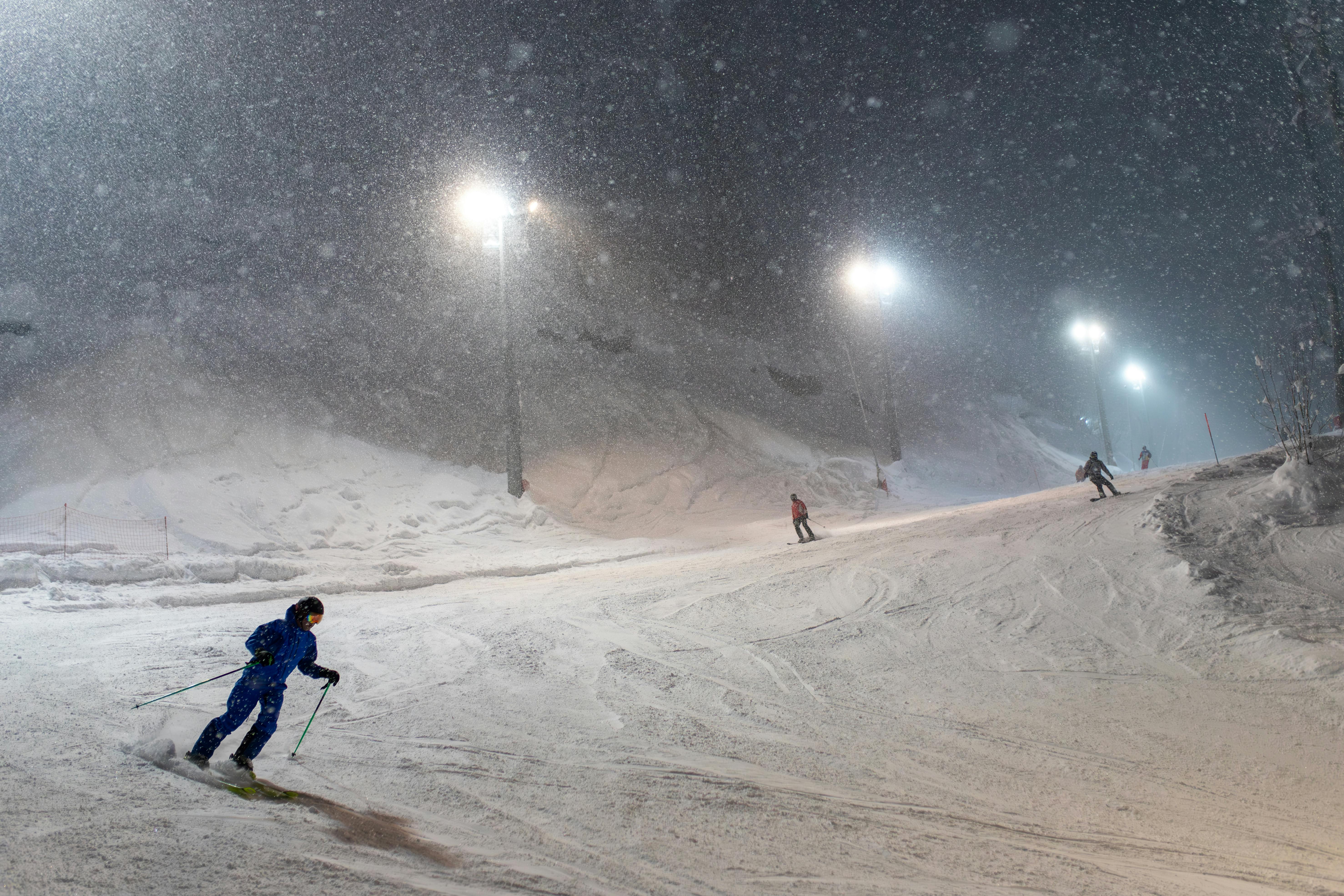 A vivid scene of skiers enjoying a snowy night on a well-lit, snow-covered mountain slope.