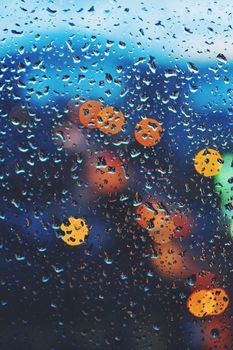 Raindrops on a window with colorful city lights in bokeh, creating a dreamy nighttime atmosphere.