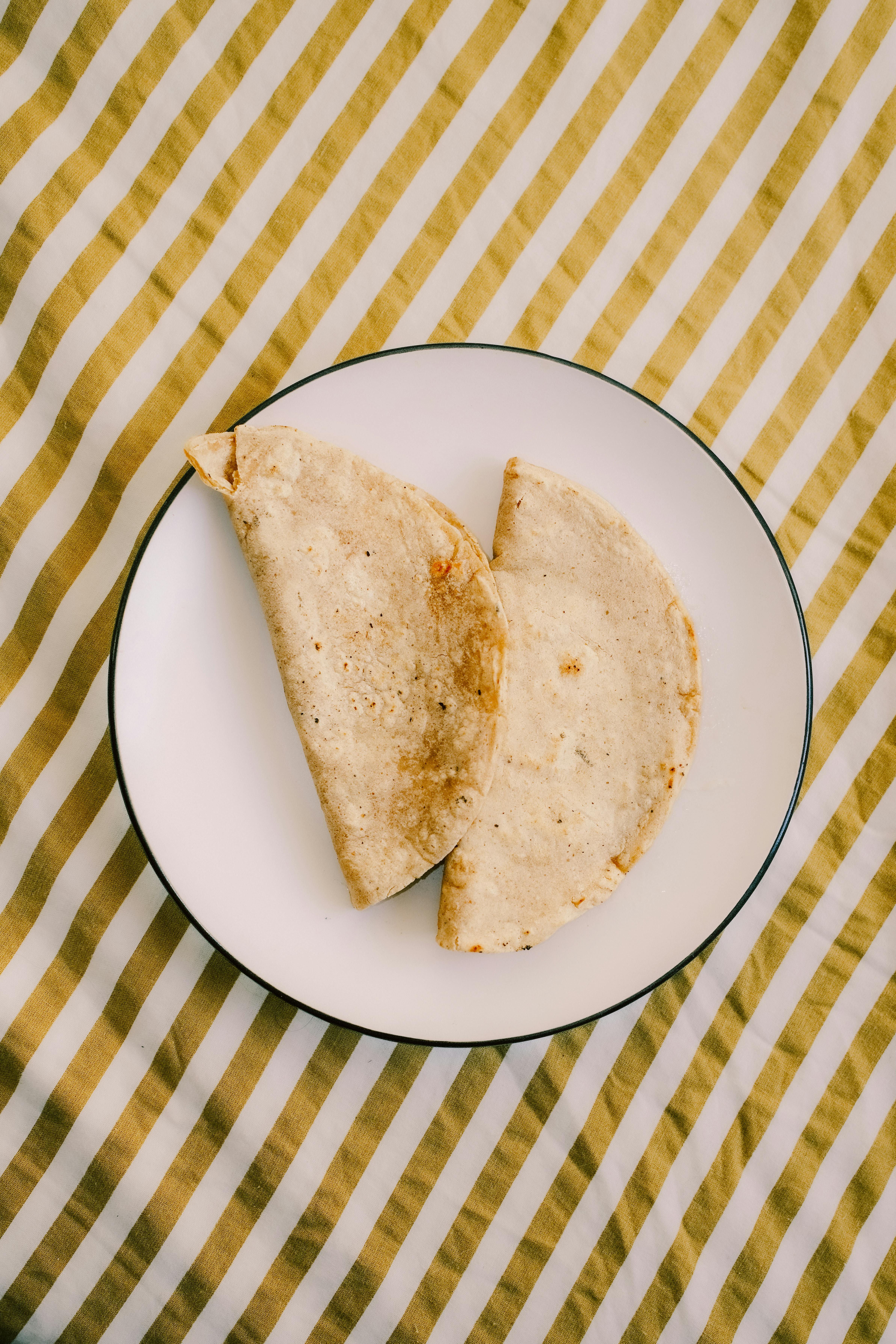 Two corn tortillas placed on a white plate, striped textile background.