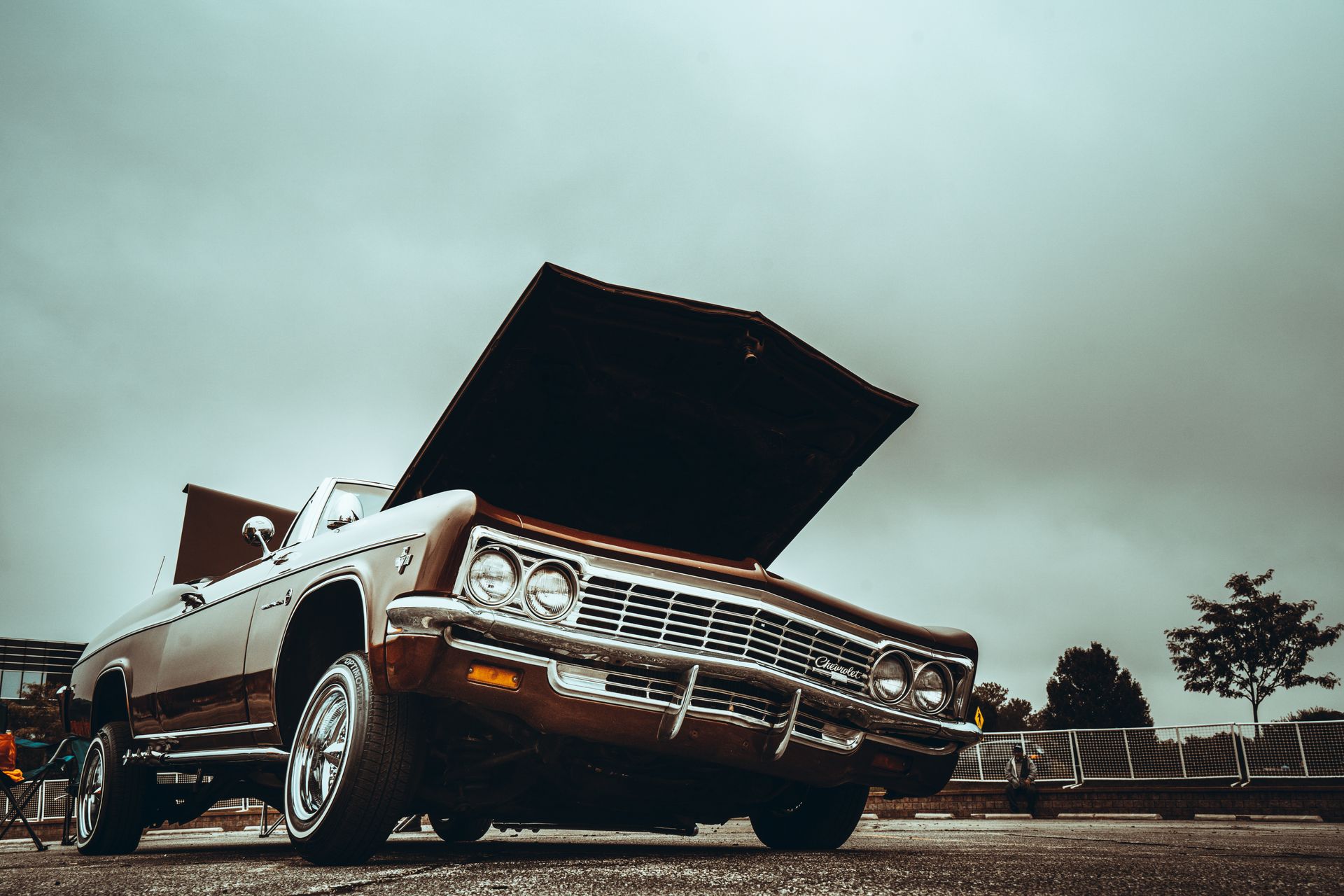 An iconic American classic car with an open hood under a moody sky, showcasing timeless elegance.