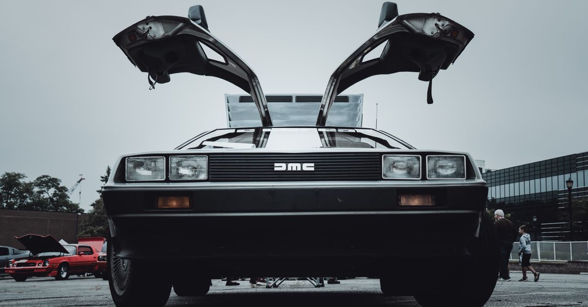 Front view of a vintage DeLorean car with its distinctive gullwing doors open, displayed outdoors.