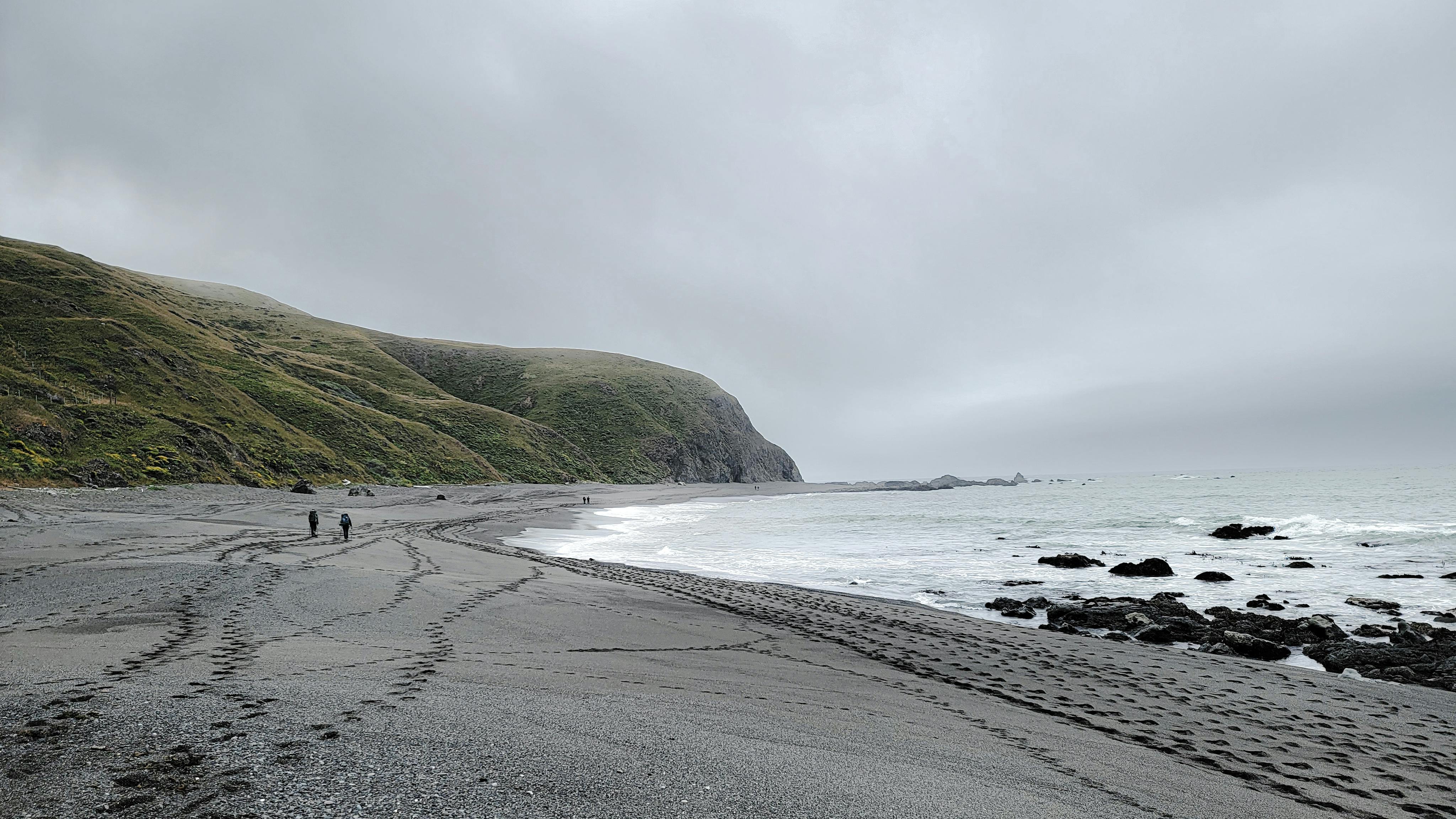 Serene coastline with footprints and rocky waves under overcast sky.