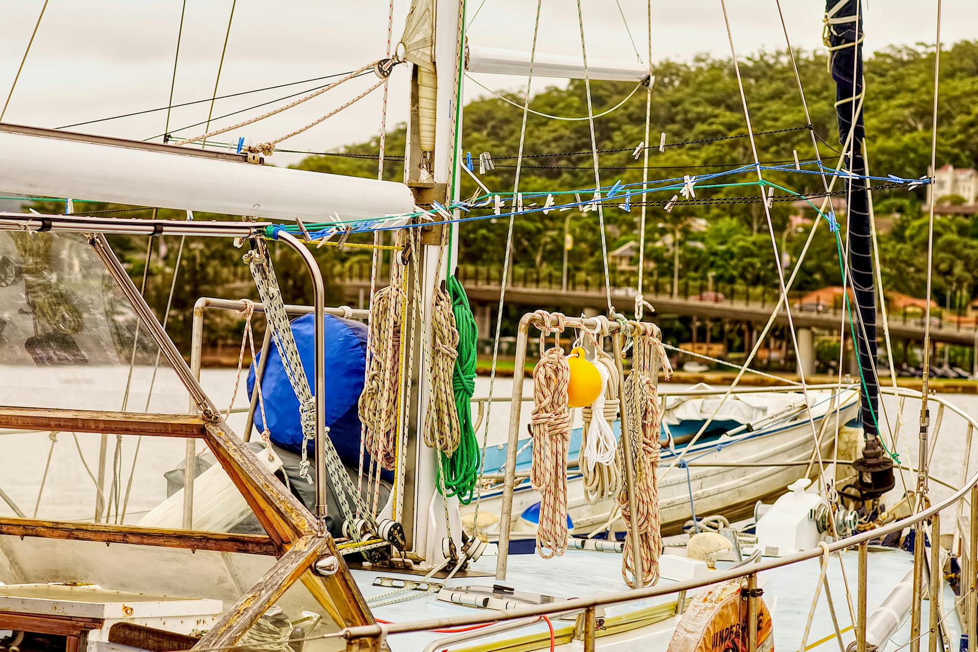 Close-up of colorful ropes and mooring equipment on a yacht docked in a marina, with lush greenery in the background.