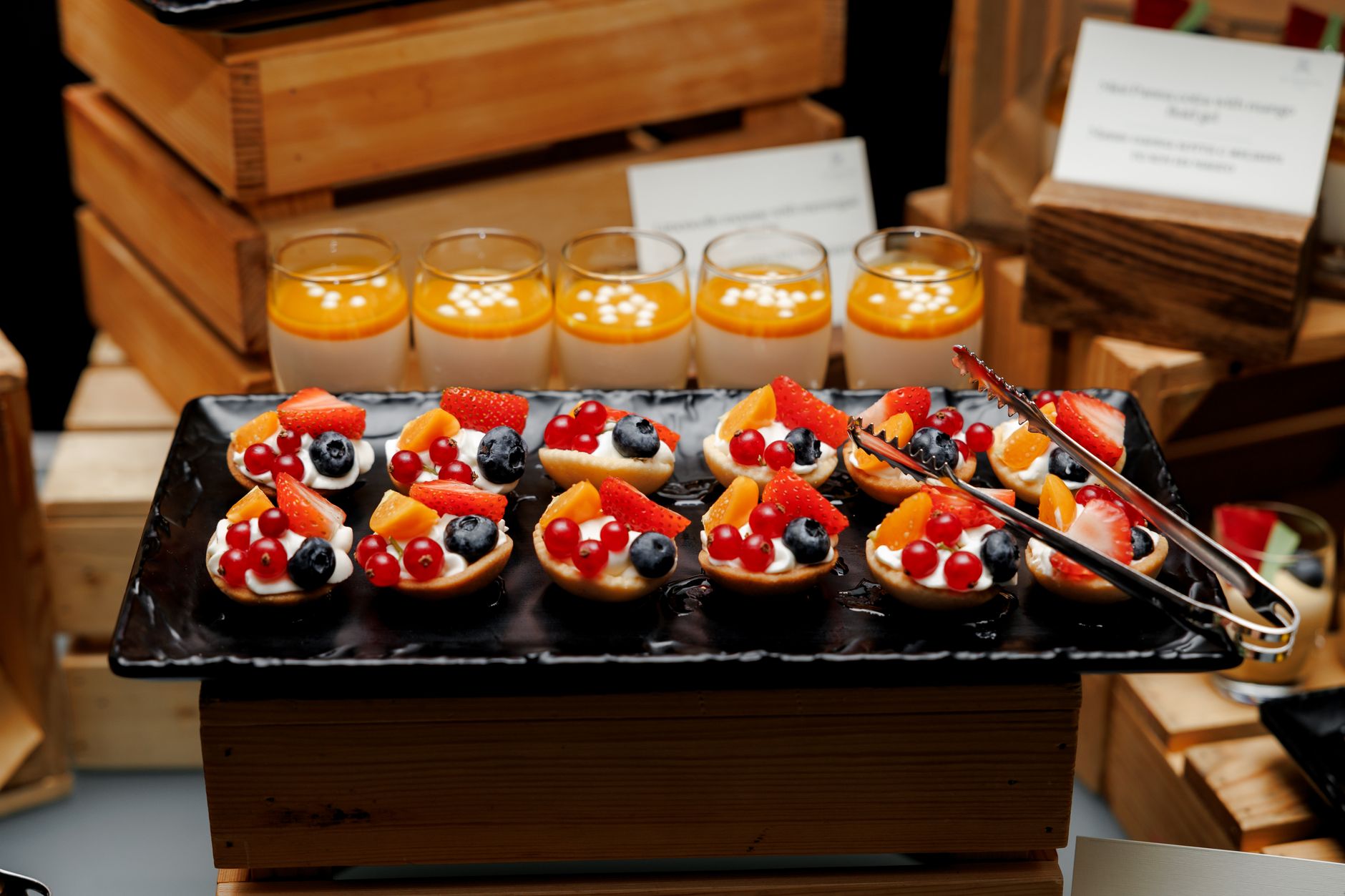 Delicious fruit tarts and mango panna cotta on a black tray at a restaurant.