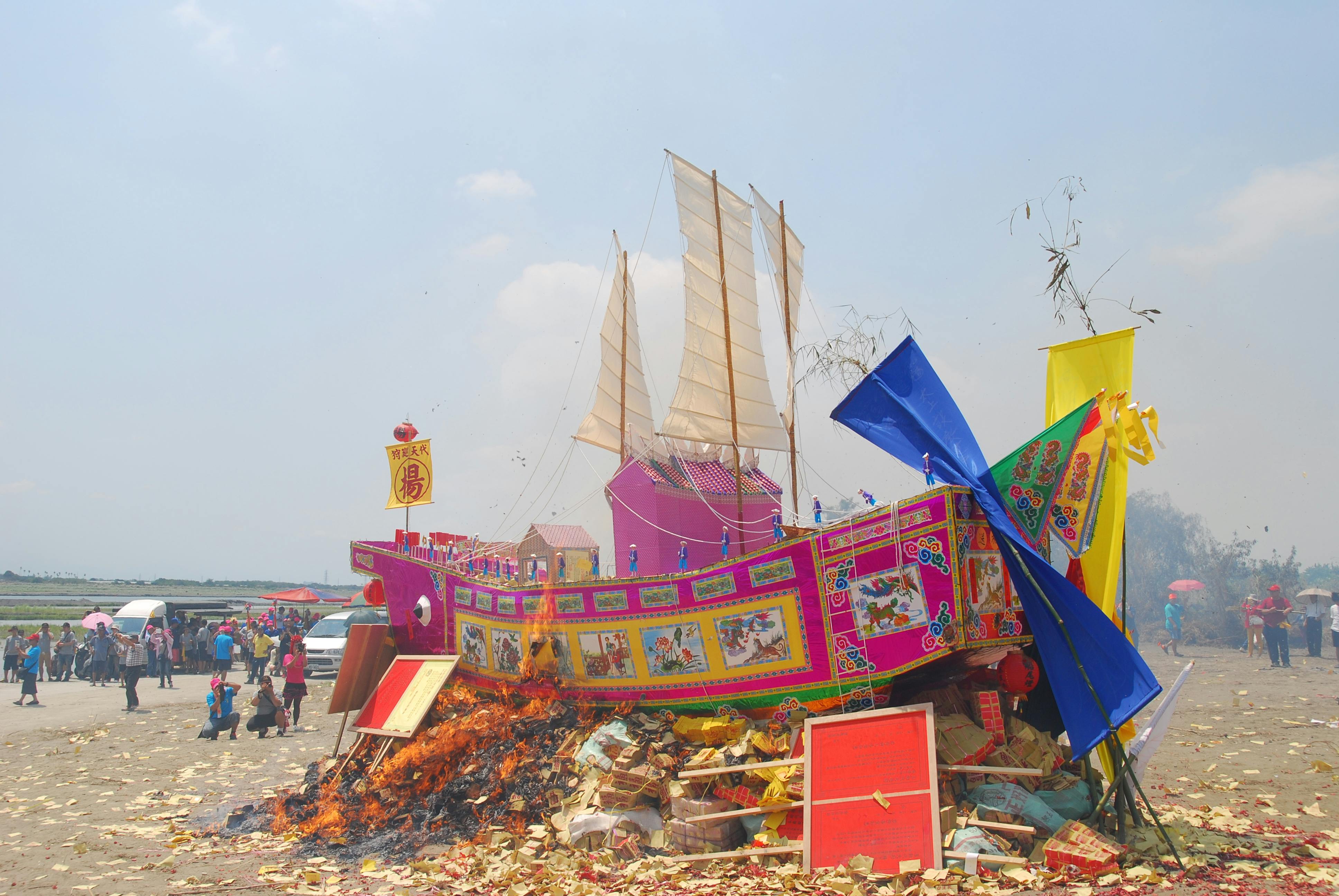 Vibrant paper ship burning during outdoor festival celebration with people gathered around.