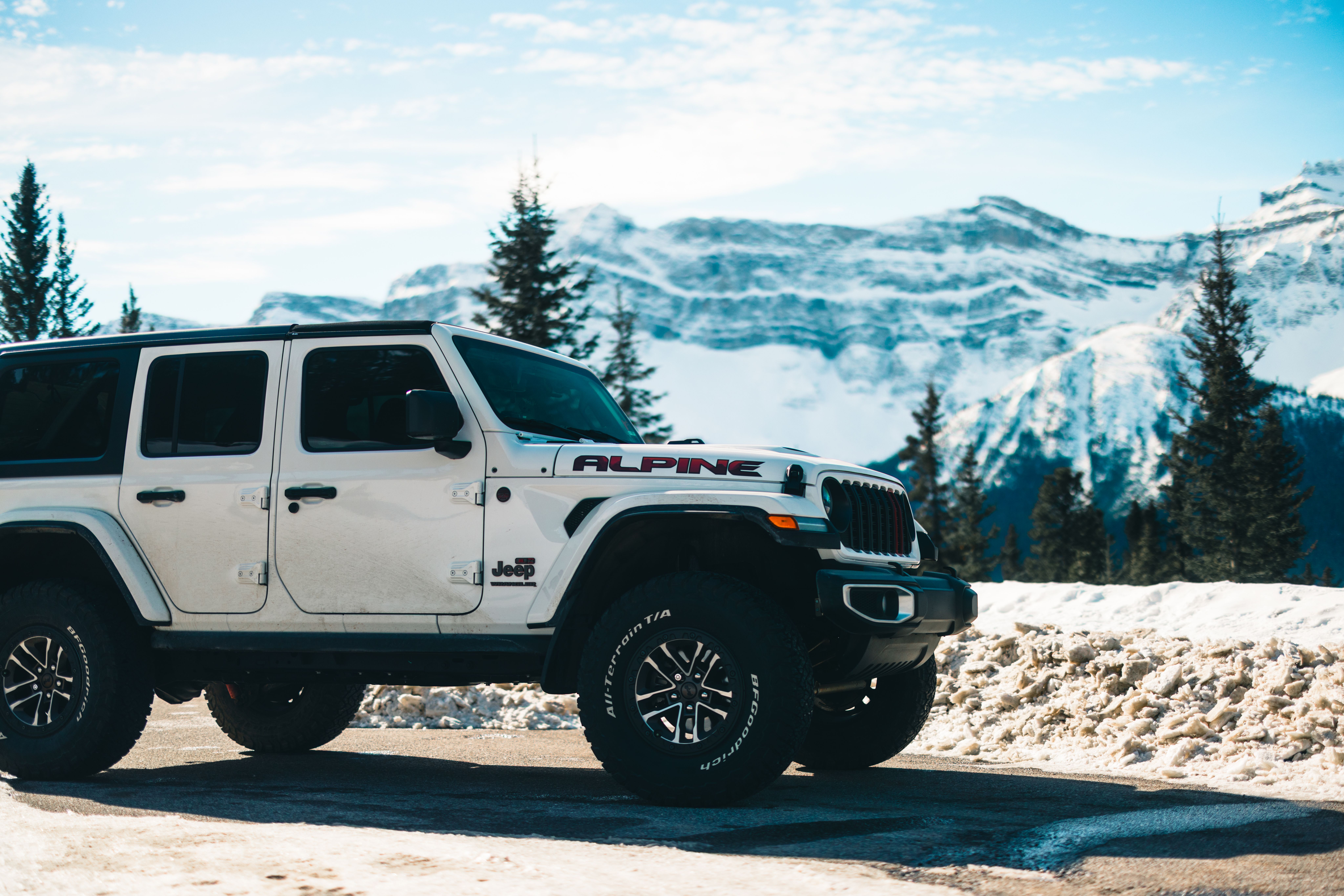A white Jeep parked on a snowy road with majestic mountain views in Jasper, Alberta.