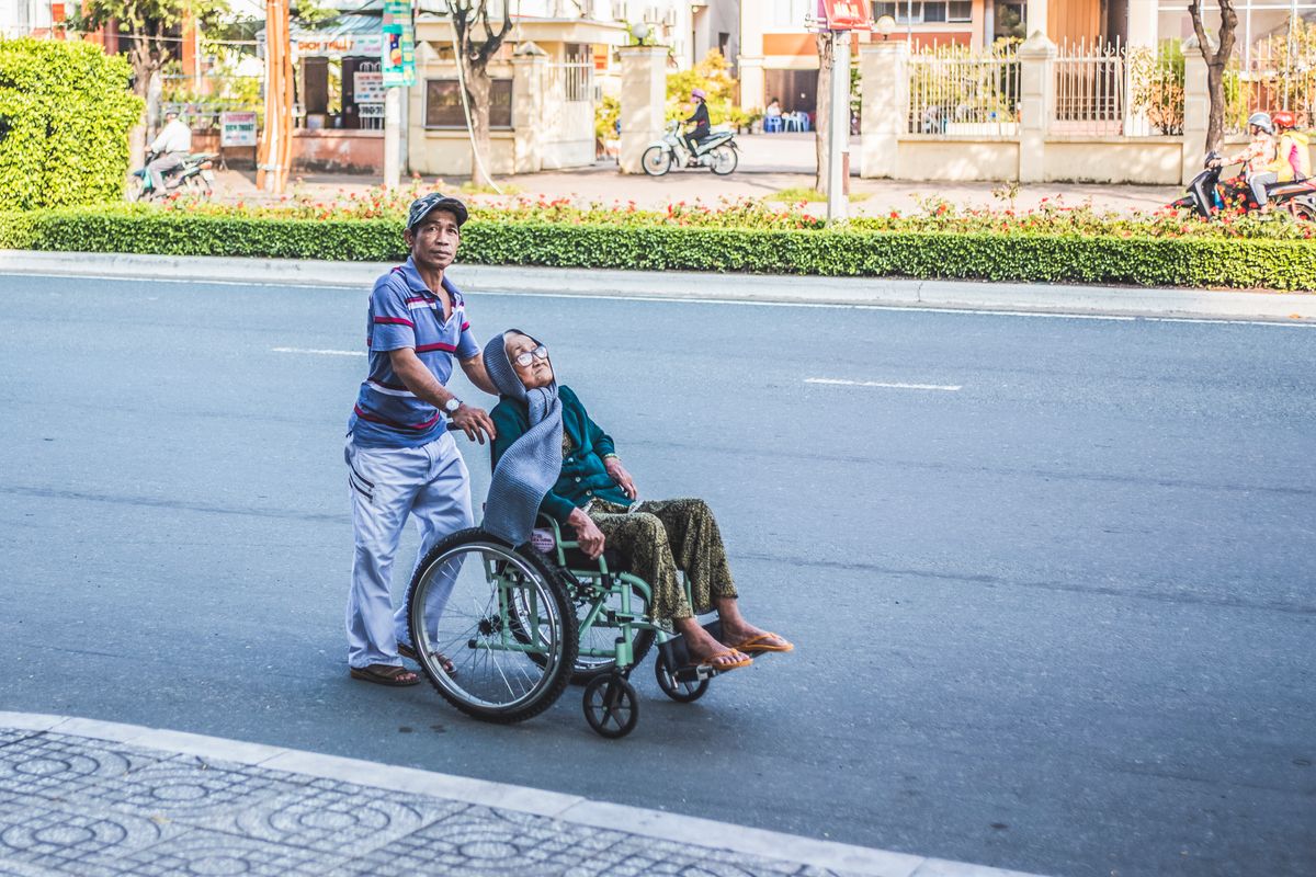 Southeast Asian carer taking an elderly relative to a clinic appointment on foot