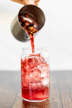 Refreshing hibiscus tea being poured over ice cubes in a clear glass, capturing a vibrant burst of color.