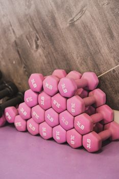 A stack of pink 3LB dumbbells arranged against a wooden wall in a gym.