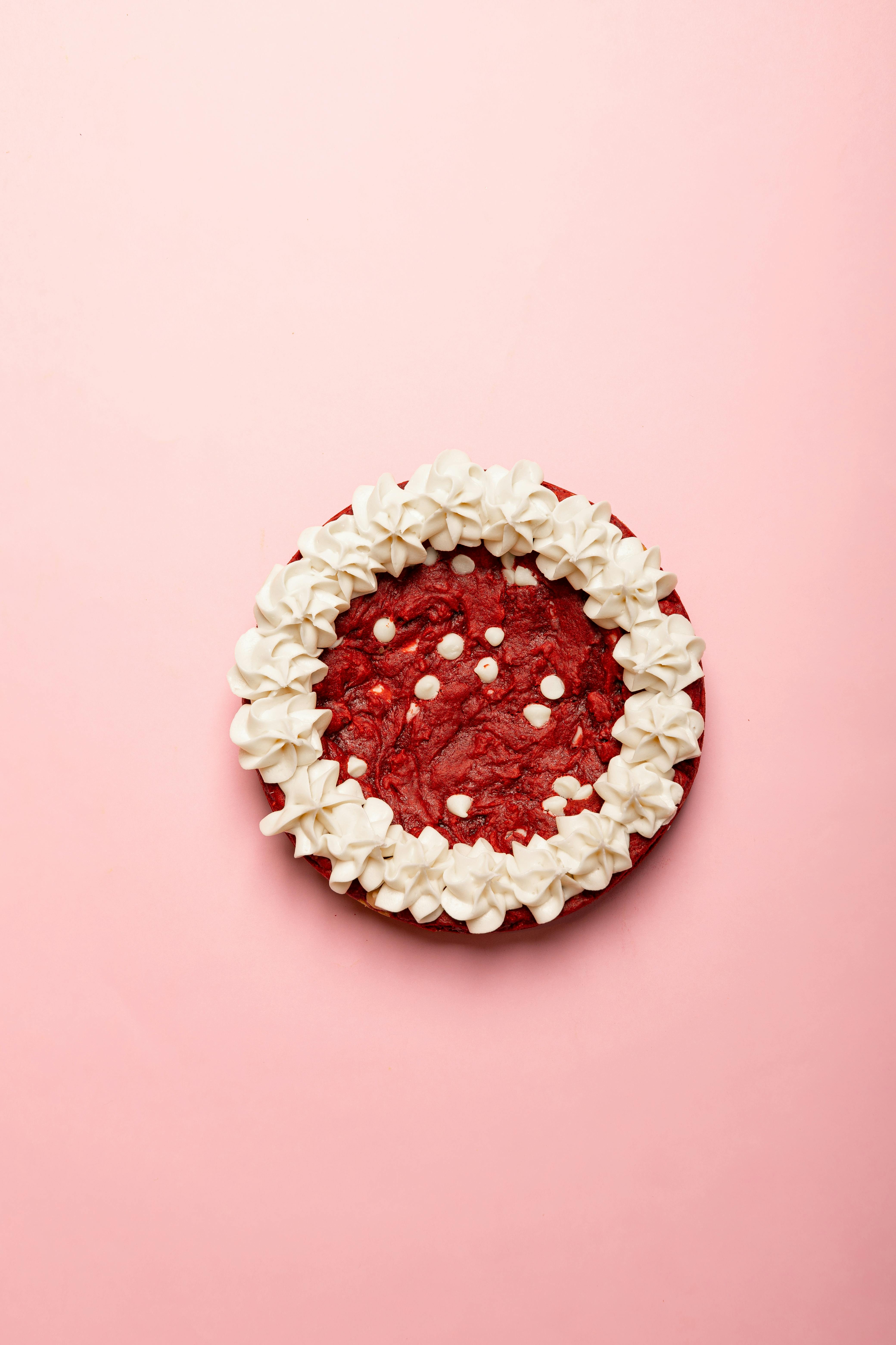 Top view of a red velvet cake with cream frosting on pink background.