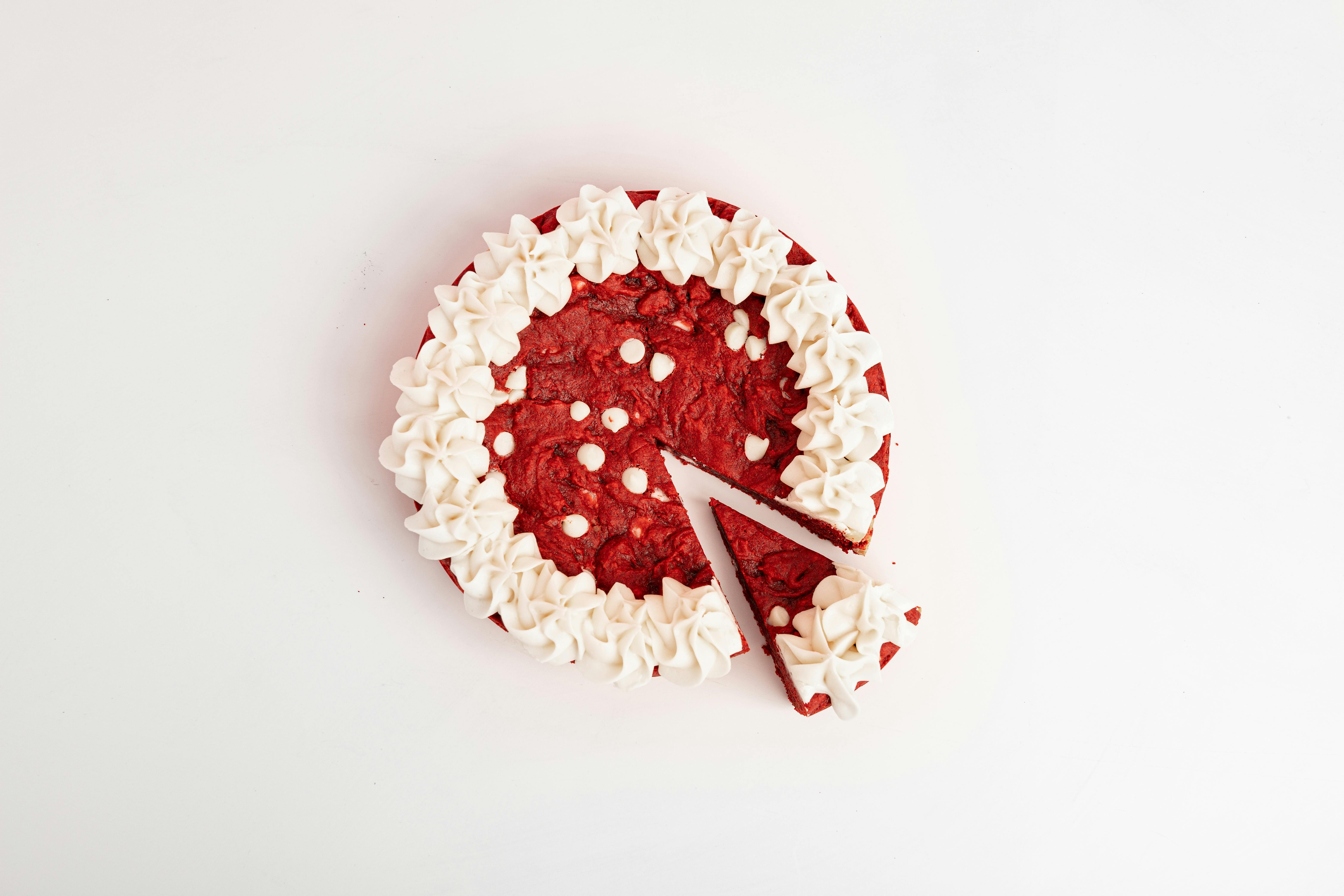 Appetizing red velvet cake with cream frosting on white background. A slice is cut out.