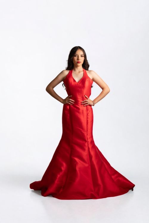 Free Portrait of a woman in a stunning red gown, posing confidently against a white backdrop. Stock Photo