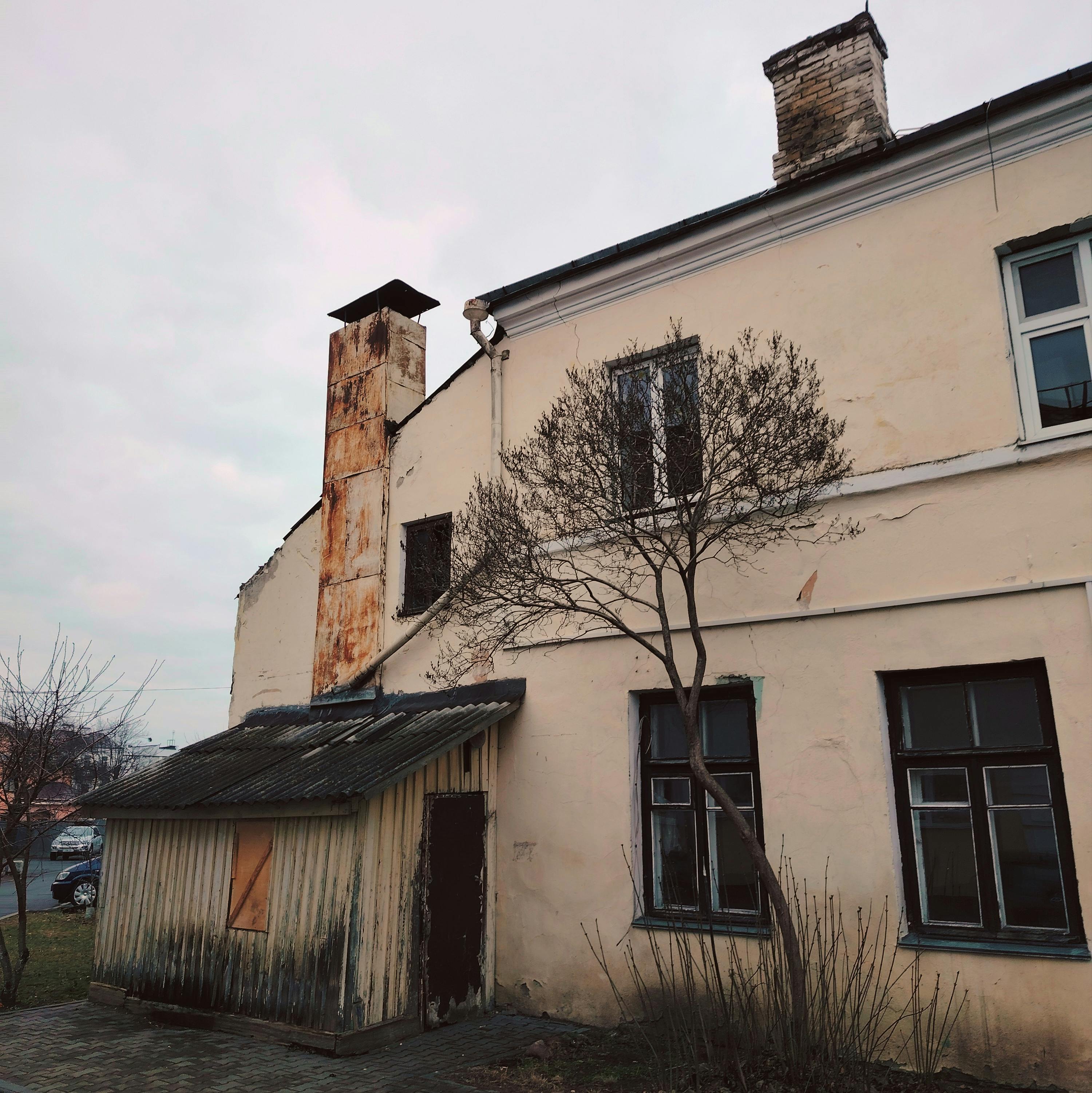 Aged house exterior with rusty chimney and bare tree, showcasing urban decay.