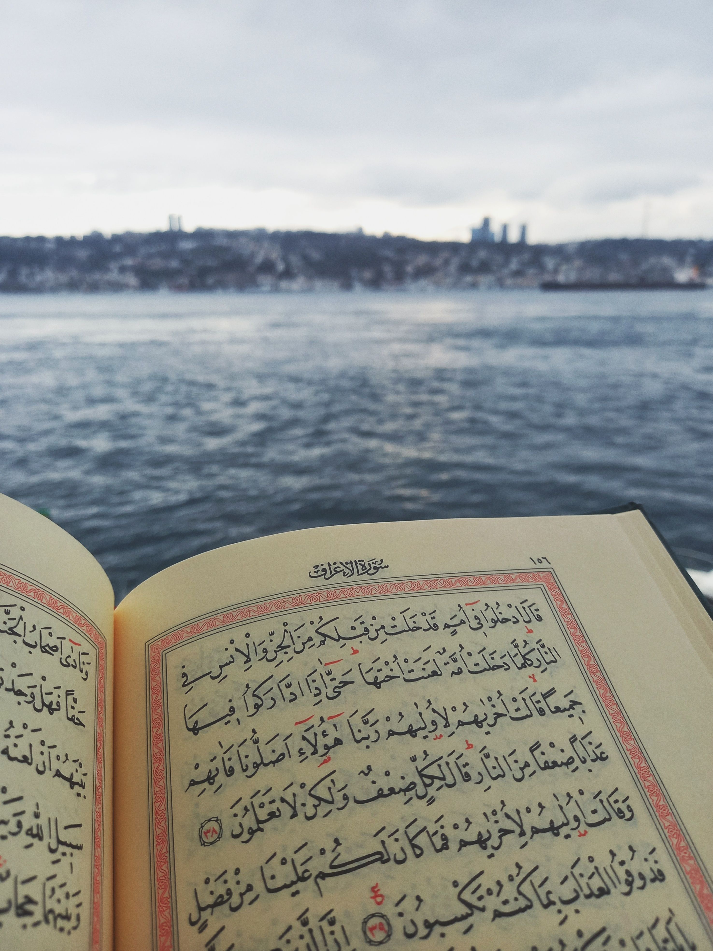 A Quran opened by the waterfront with a city in the distant horizon.