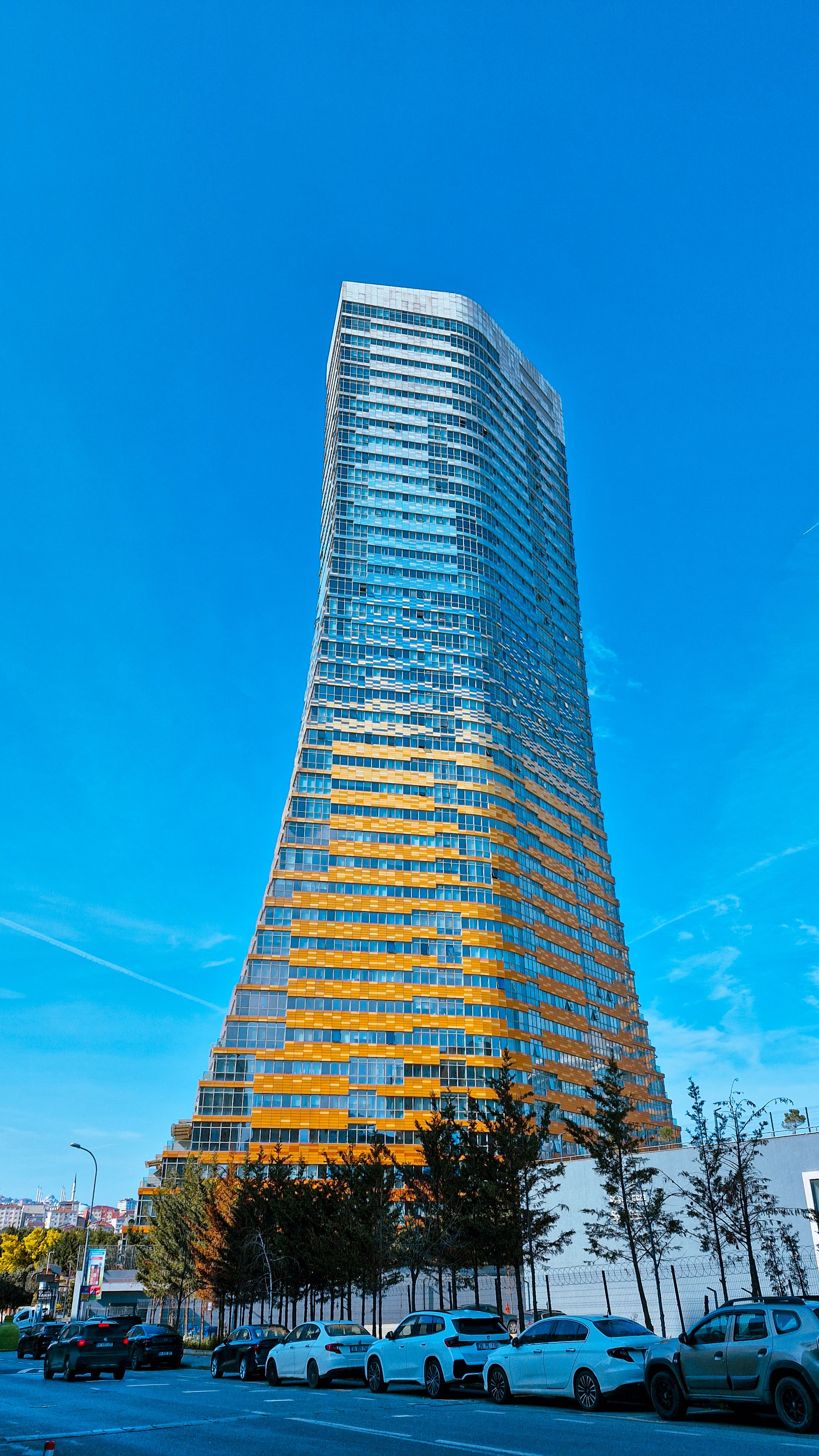 Tall, modern skyscraper with reflective glass facade against a clear blue sky, showcasing urban architecture.