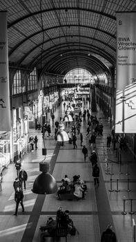 People bustling inside Wroclaw Train Station with arched glass roof.