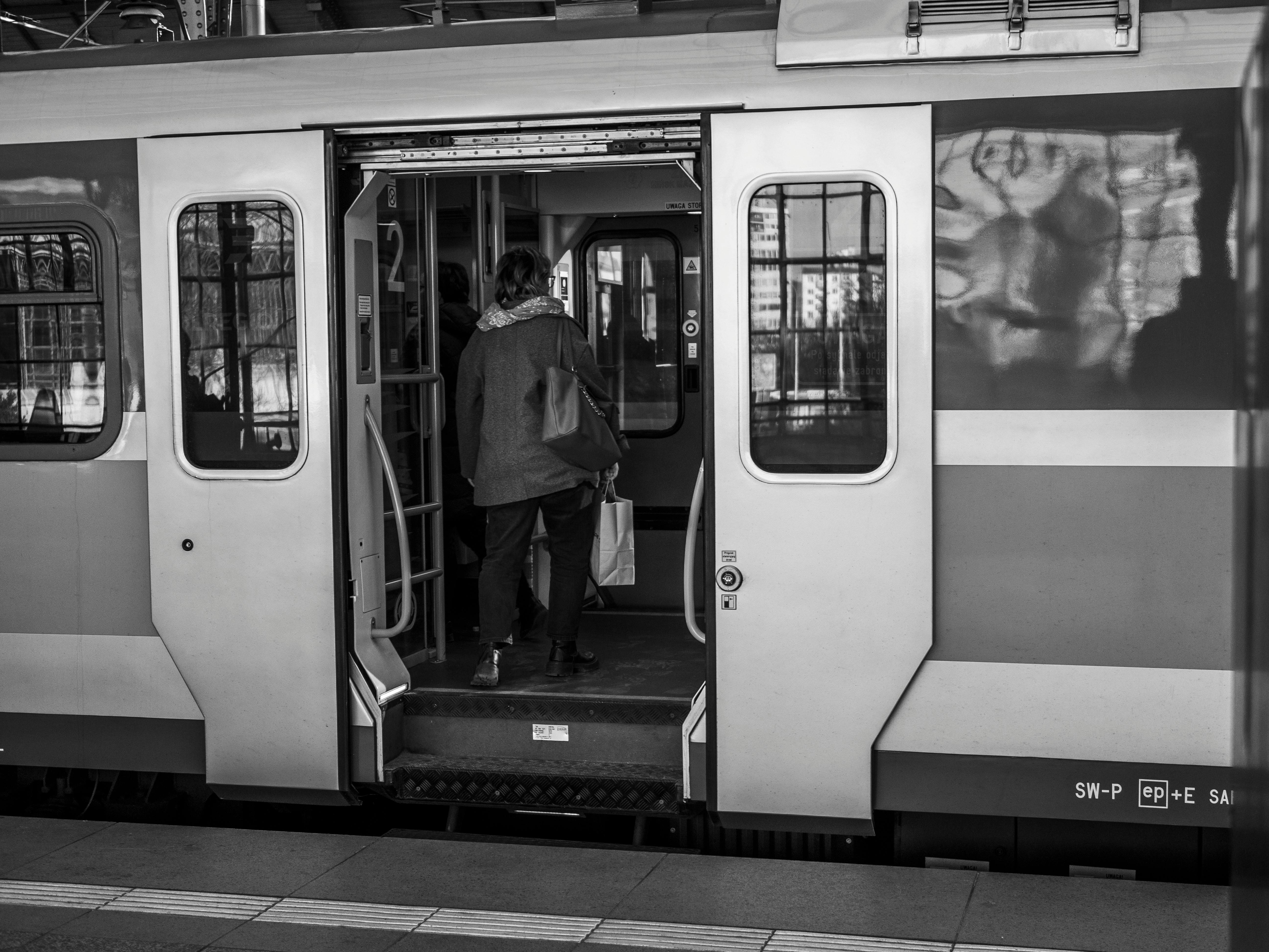 An individual boards a train at a station in a black and white setting. Captures urban transit.