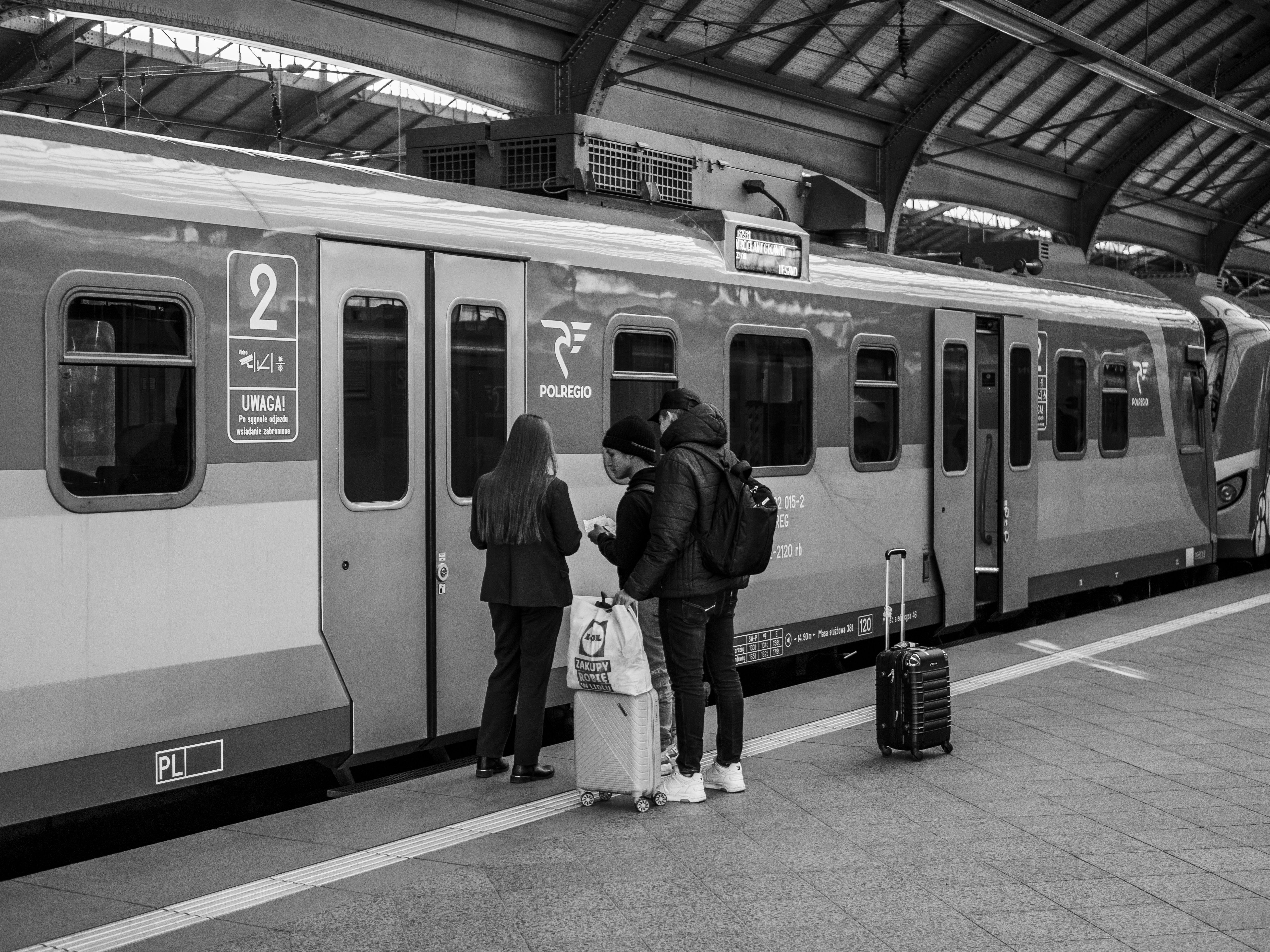 Monochrome image of travelers boarding a POLREGIO train at a station.