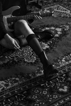 Black and white photo of a woman sitting on a rug, holding an electric guitar.