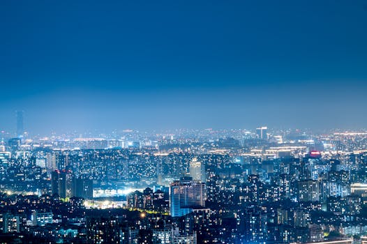 Panoramic view of a bustling city skyline illuminated at night, showcasing urban development and vibrant lights.