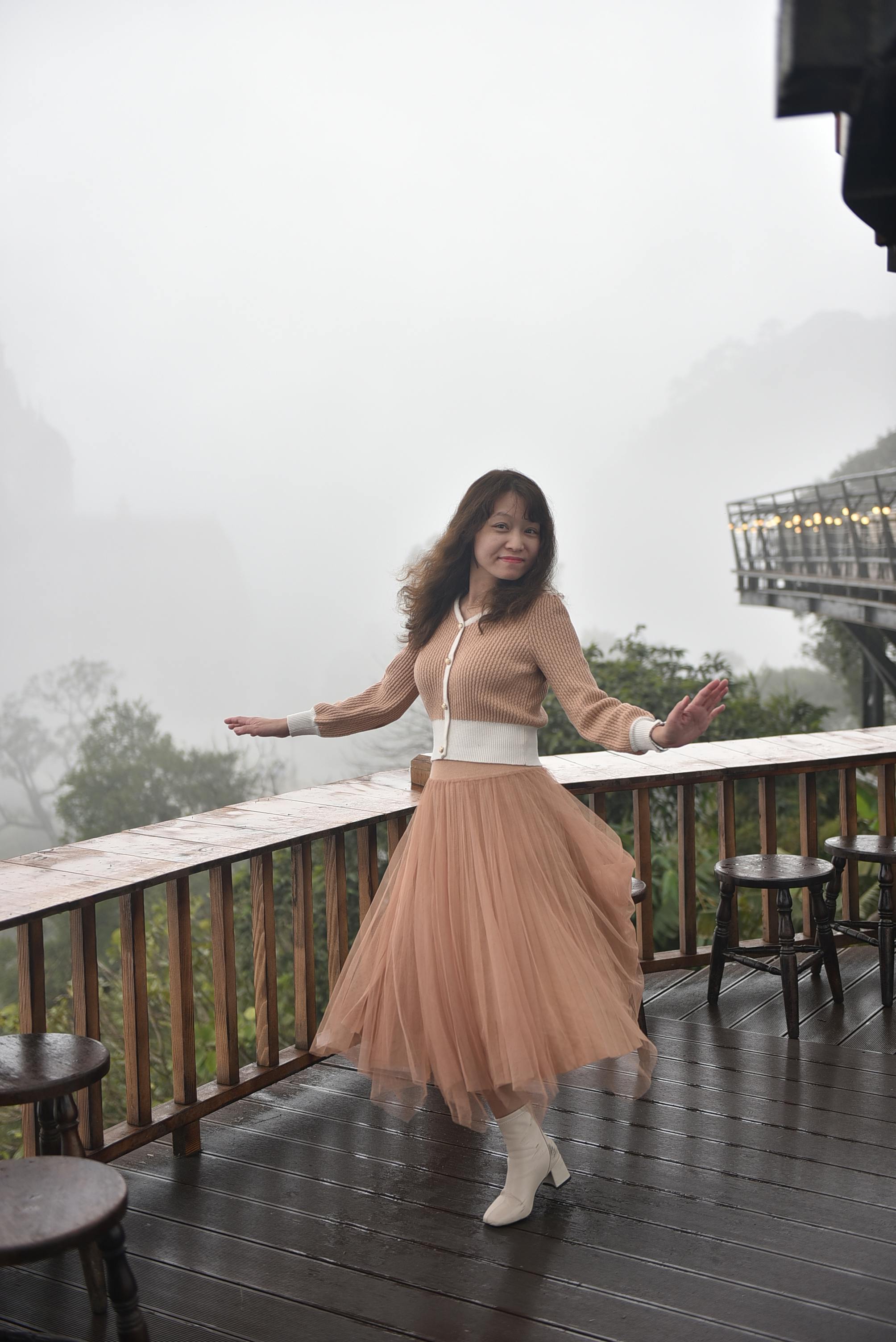 Woman in flowing skirt spins joyfully on a misty outdoor terrace.