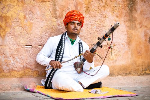 Free A Rajasthani musician plays the rawanhatta, showcasing cultural heritage against a textured wall. Stock Photo