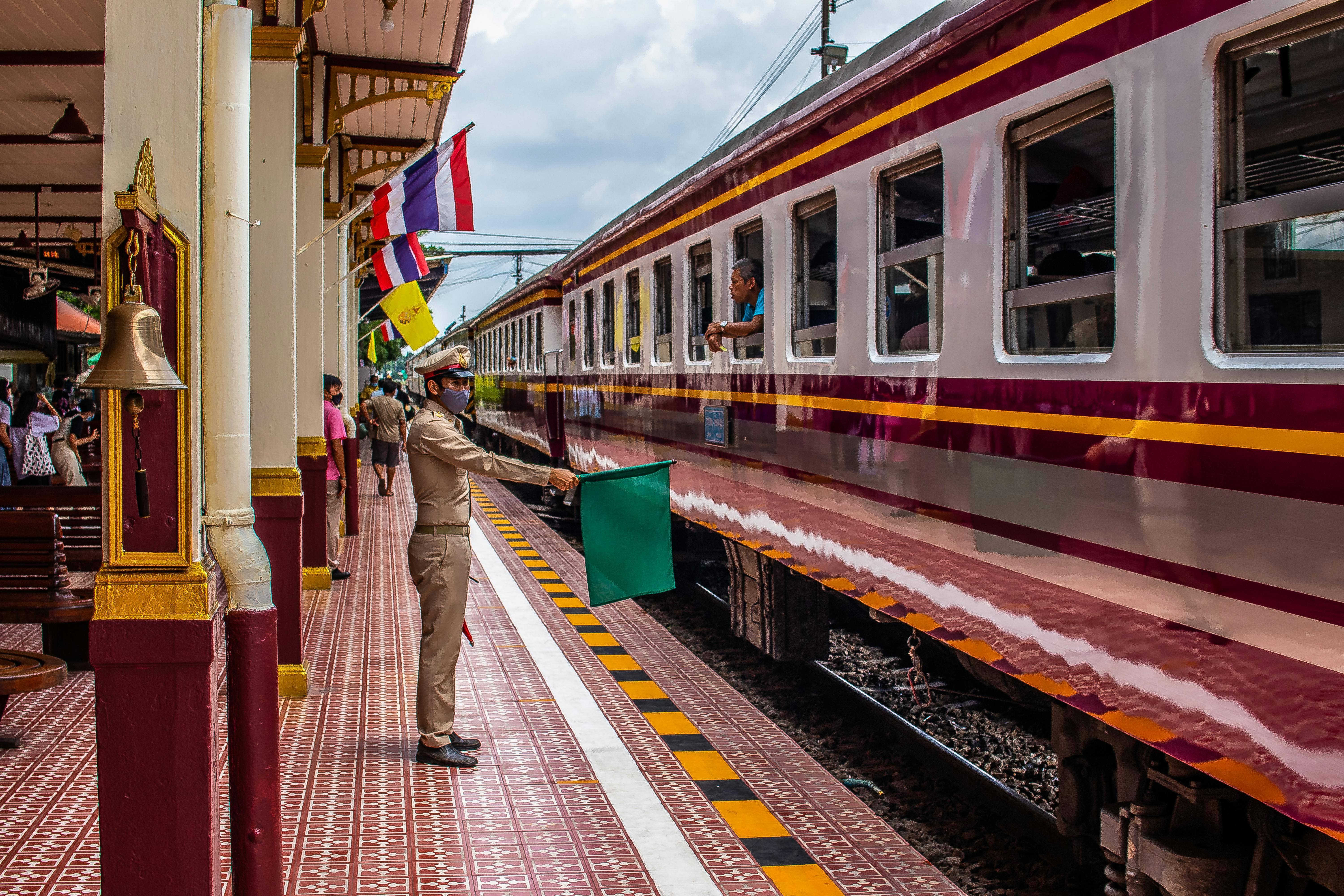 Conductor directing train at Ayutthaya Railway Station in Thailand, vibrant travel scene.