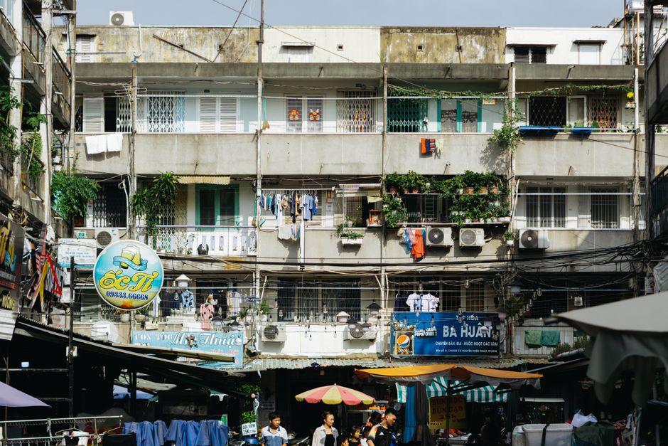 Colorful urban market scene with bustling crowd in front of a vintage apartment block.