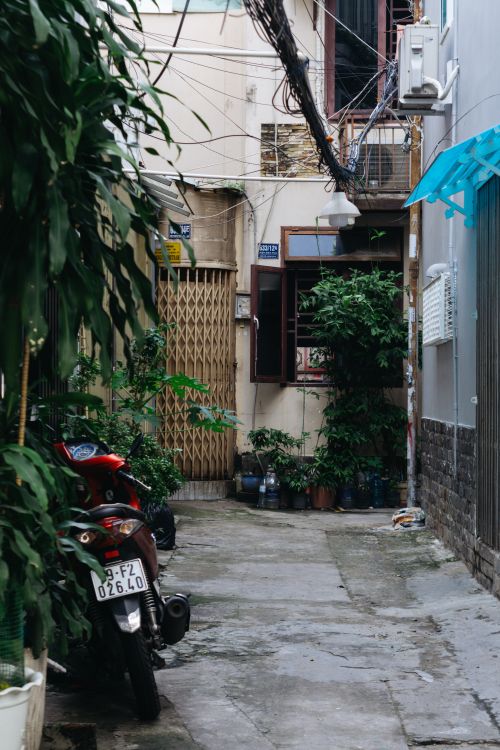 Free A narrow alleyway with a motorcycle and lush plants, showcasing urban life. Stock Photo
