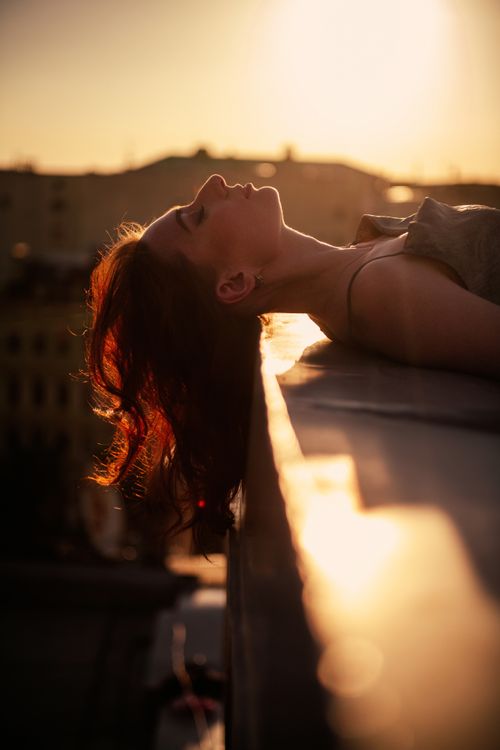 Free A serene portrait of a woman relaxing on a rooftop ledge during sunset, embodying tranquility. Stock Photo