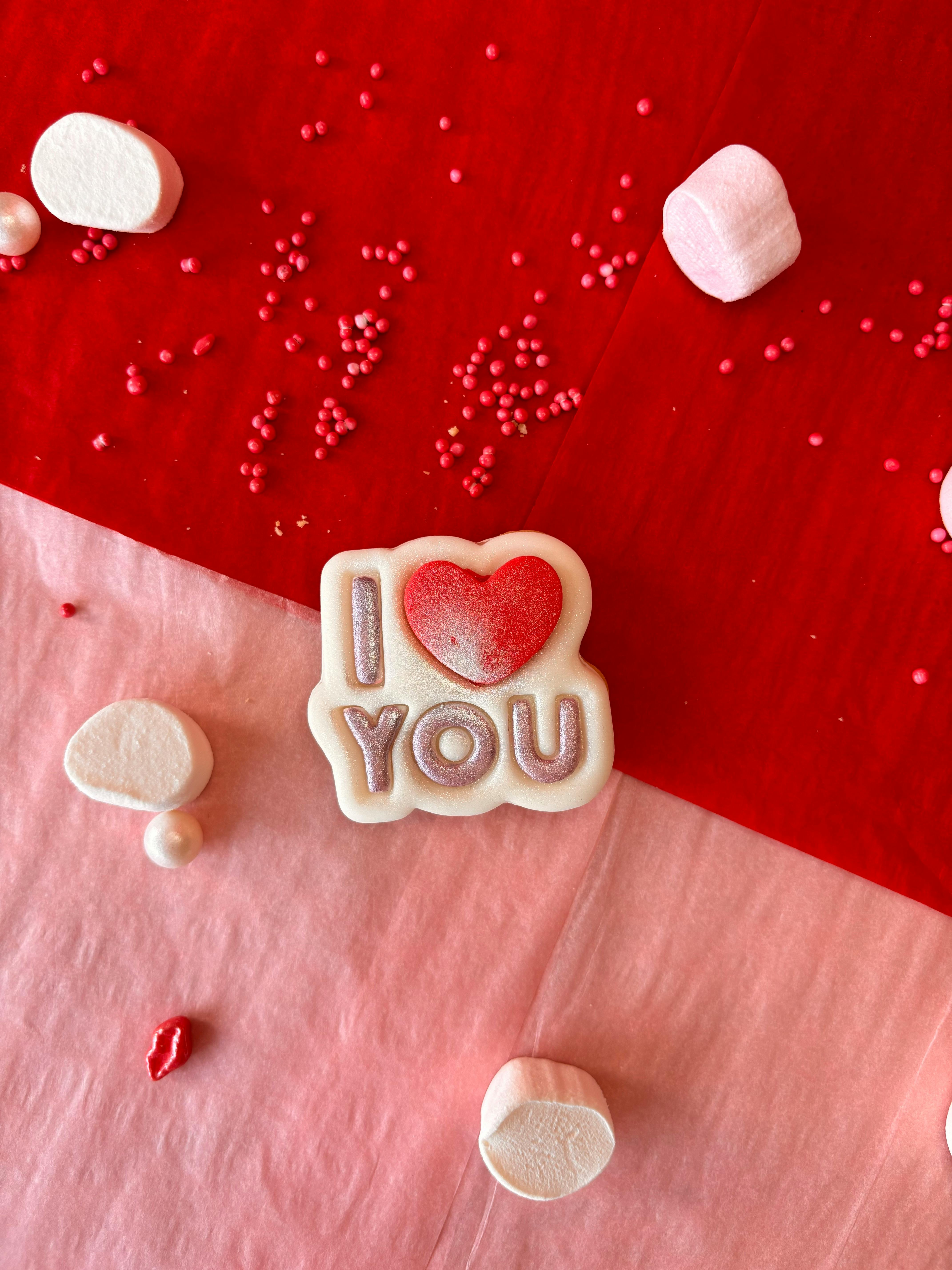 Heart-themed candy surrounded by red sprinkles on a red and pink background.