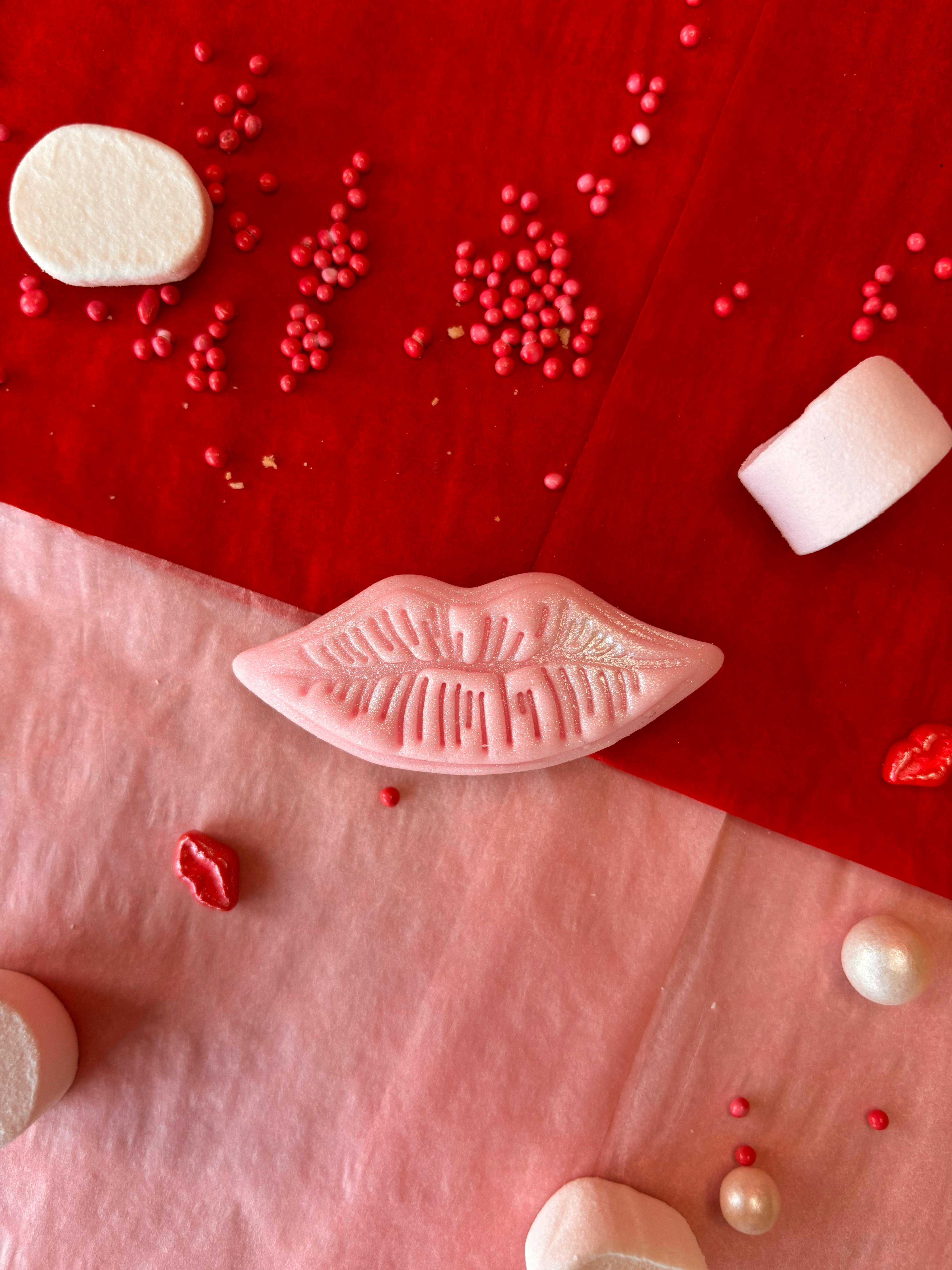 Flat lay of pink lips-shaped candy with marshmallows on vibrant red and pink backdrop.