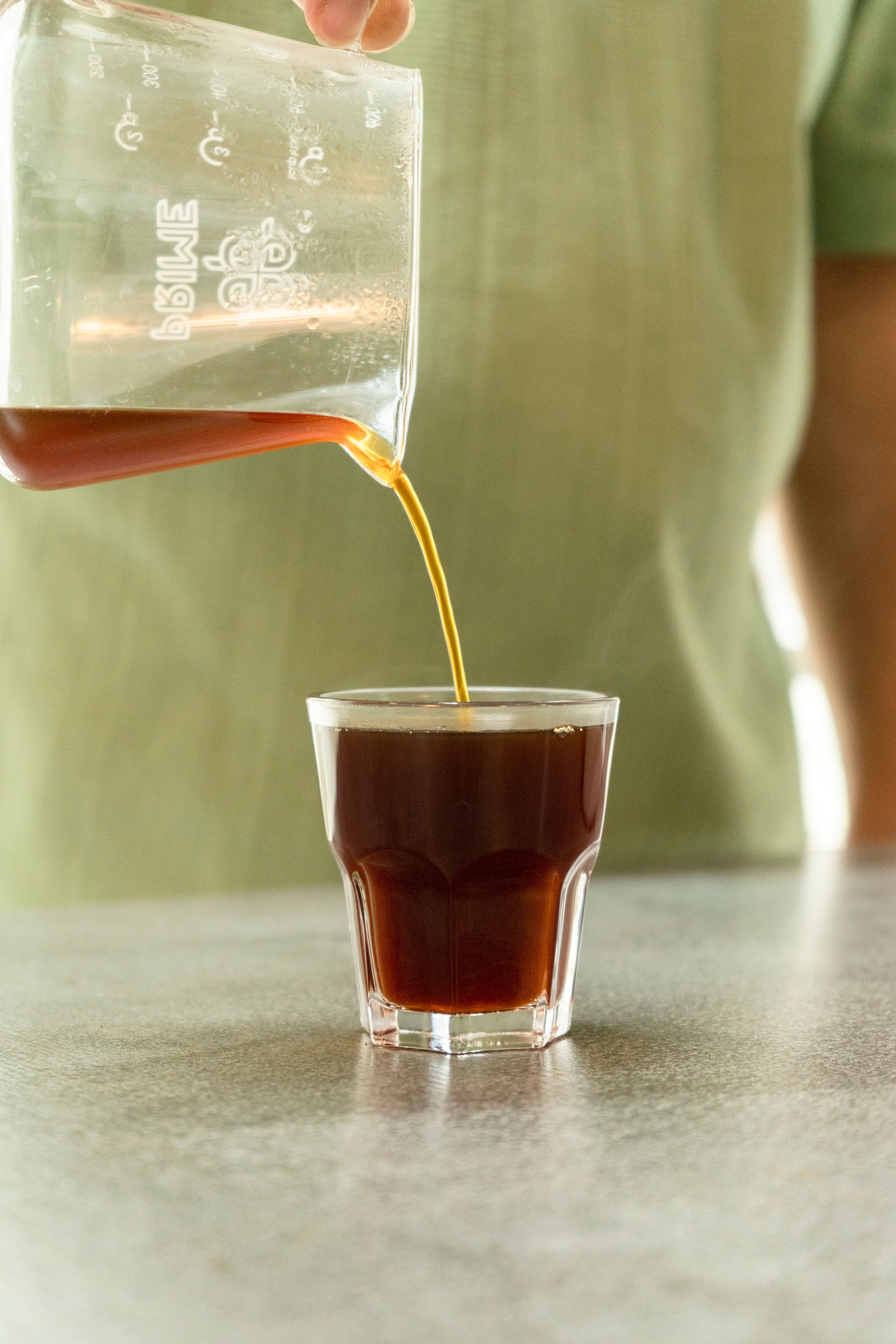 Fresh coffee being poured into a glass cup from a beaker.