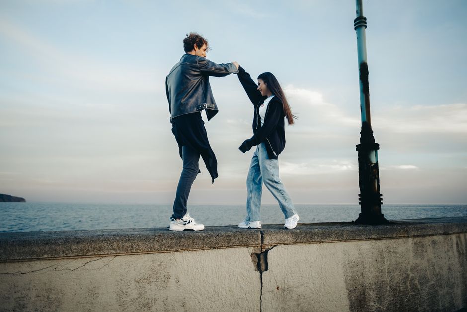 A joyful couple dances on a seaside wall, capturing a moment of happiness at sunset.