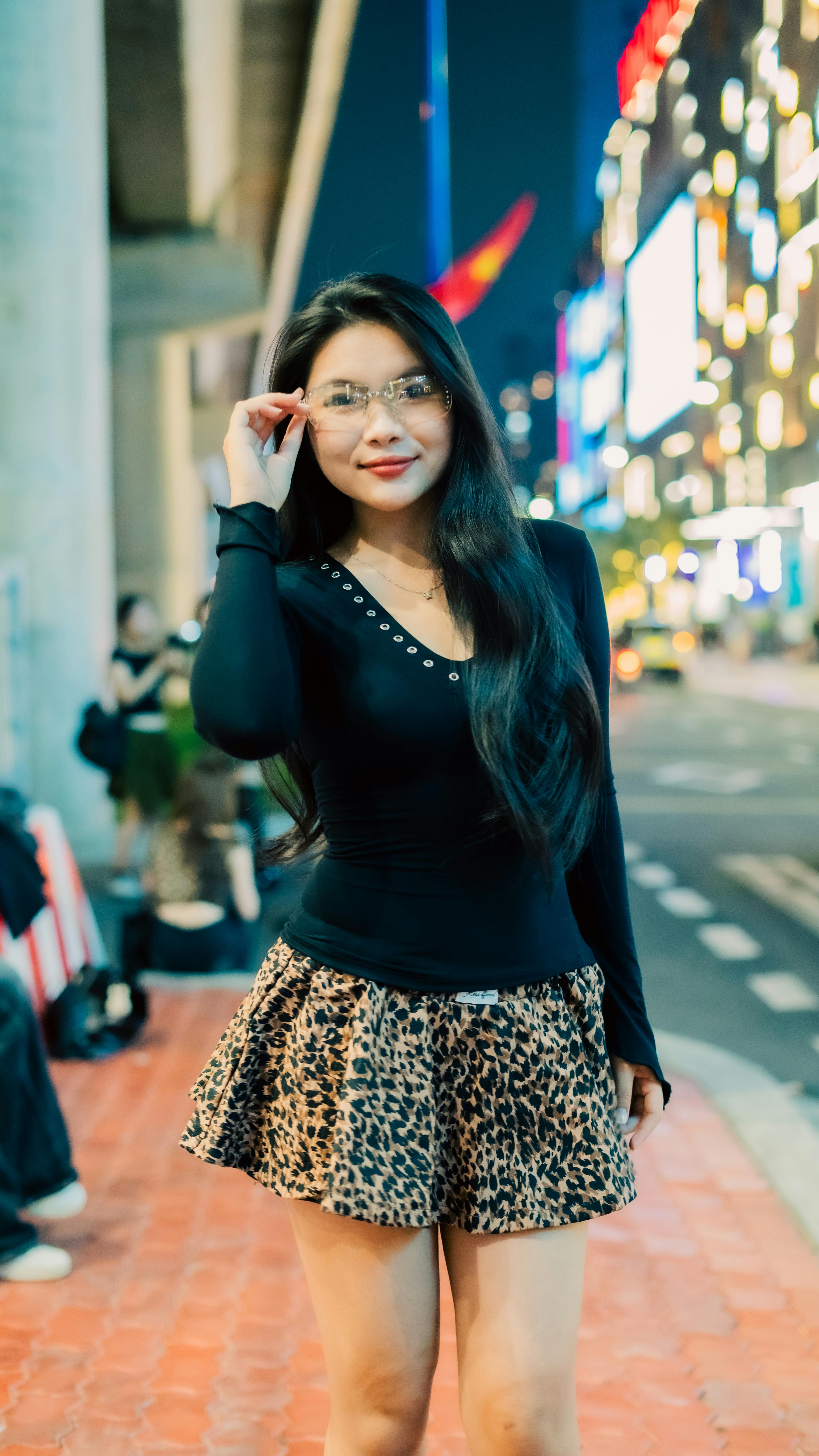 Elegant woman in leopard print skirt standing on a lively urban street at night.
