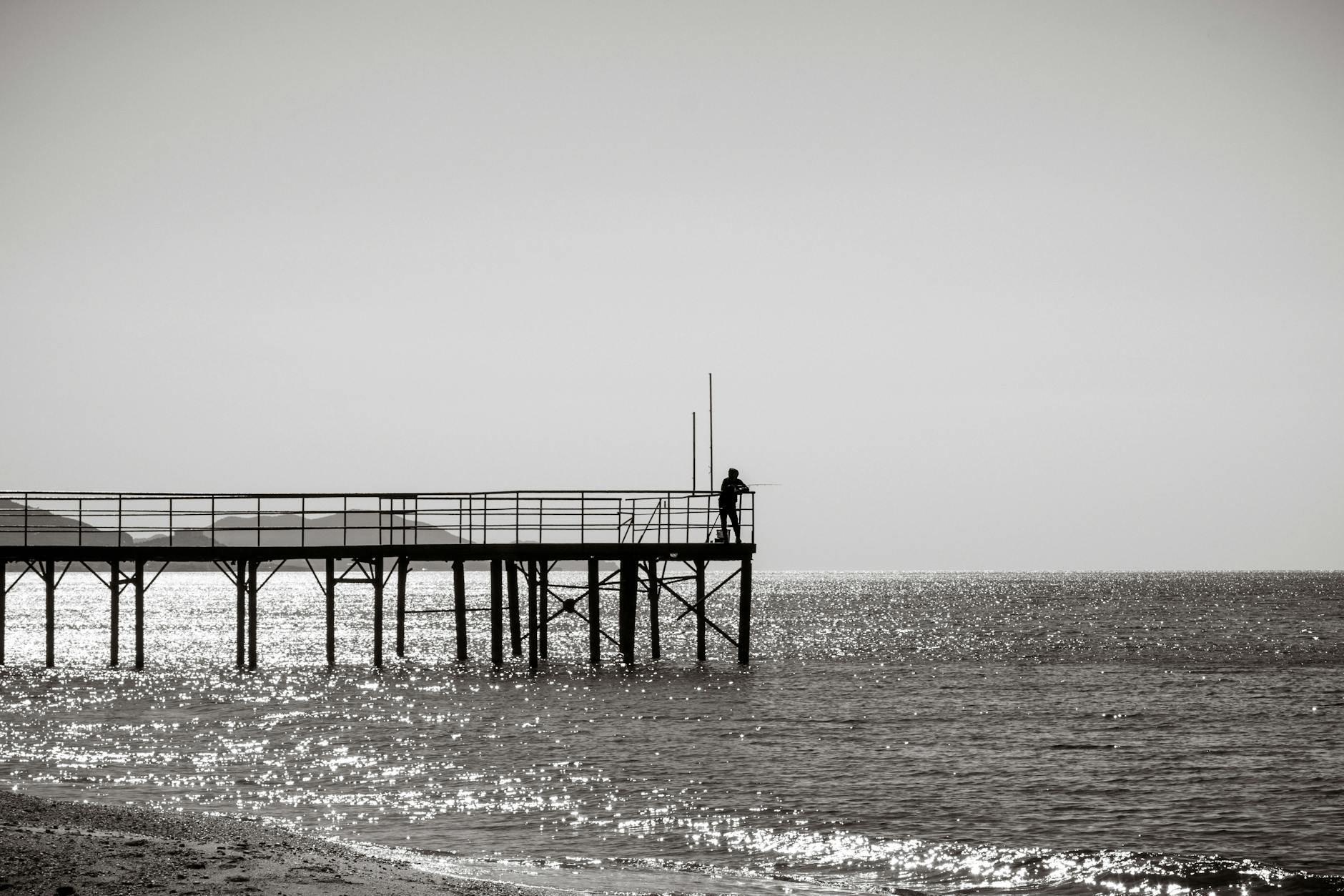 A lone fisherman on a wooden pier in Alanya, Antalya, Türkiye during a tranquil sunrise.