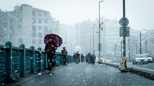Free A bustling city bridge during a snowfall, with pedestrians and colorful umbrellas. Stock Photo