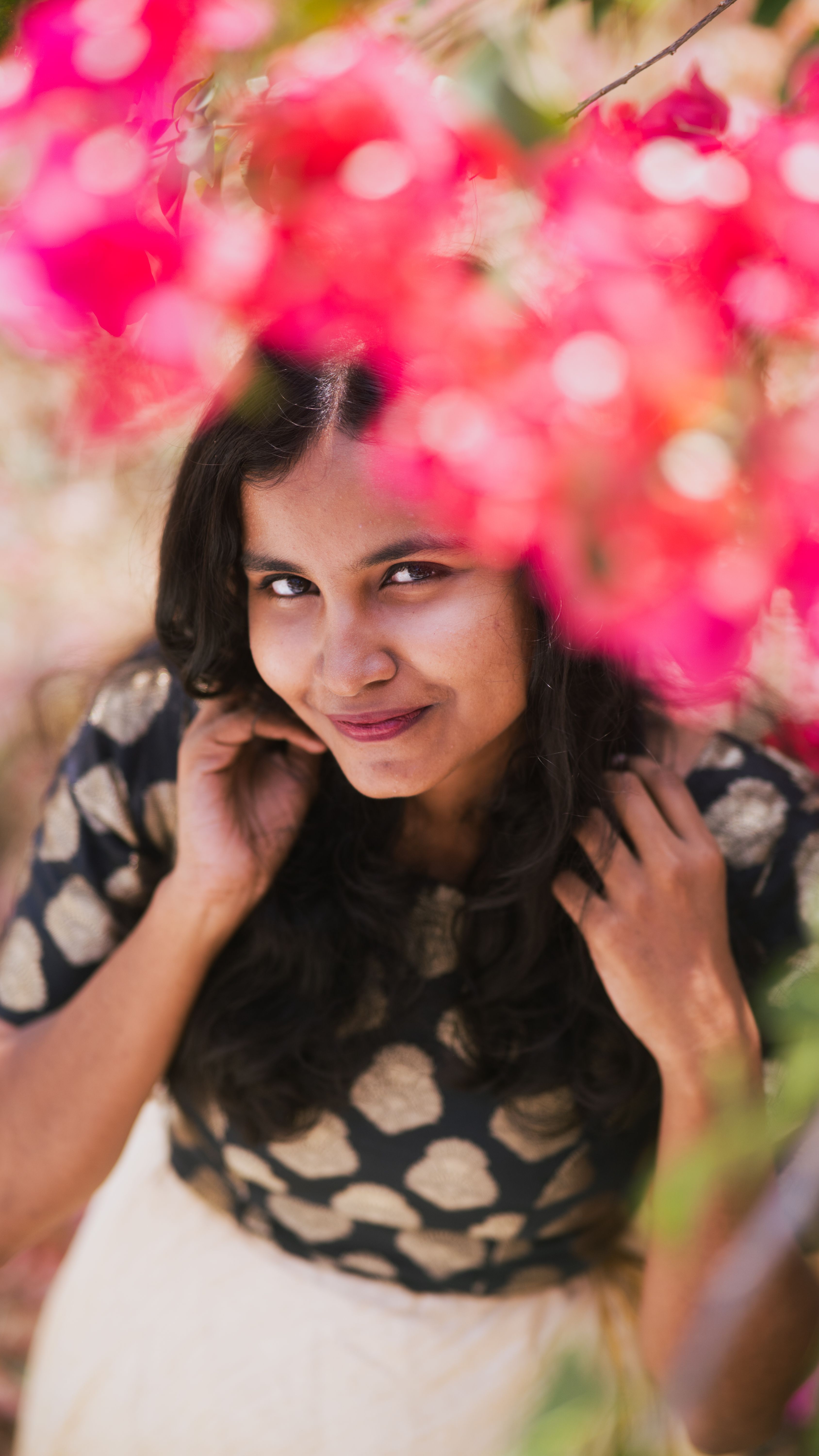 A young woman smiles warmly amidst bright pink flowers, creating a cheerful and vibrant portrait.