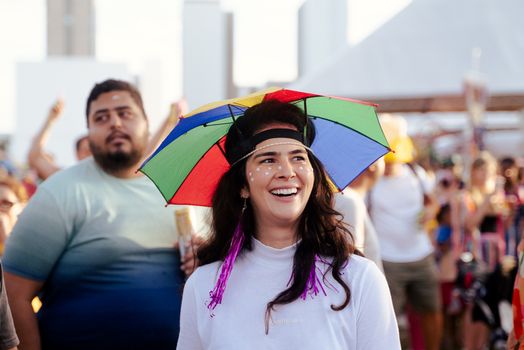 Cheerful woman with rainbow umbrella hat enjoying a vibrant outdoor festival.