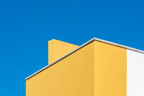 Free Crisp minimalist shot of geometric architecture with bold yellow walls and clear blue sky. Stock Photo