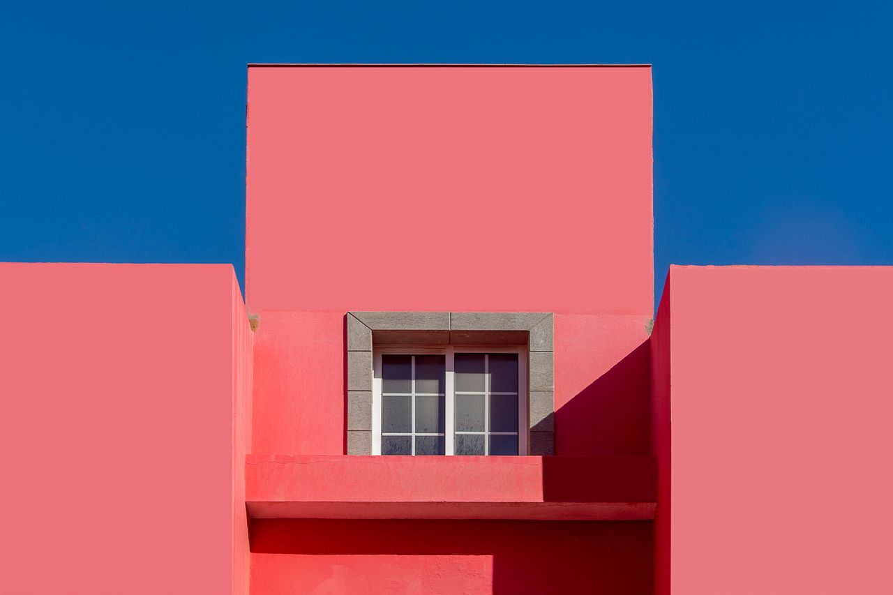 a minimalist facade featuring a vibrant red wall against a clear blue