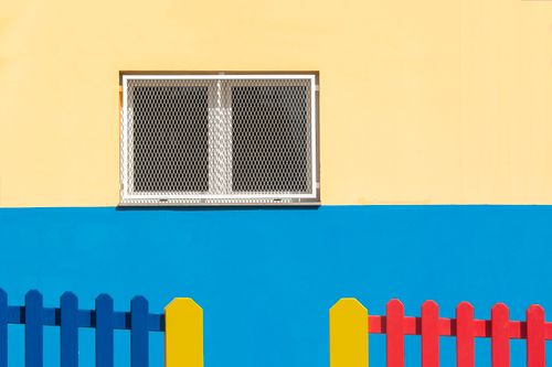 Free Vibrant facade featuring a barred window and a colorful picket fence in modern minimalistic style. Stock Photo