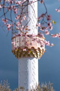 A picturesque view of a minaret surrounded by vibrant cherry blossoms under a clear spring sky.