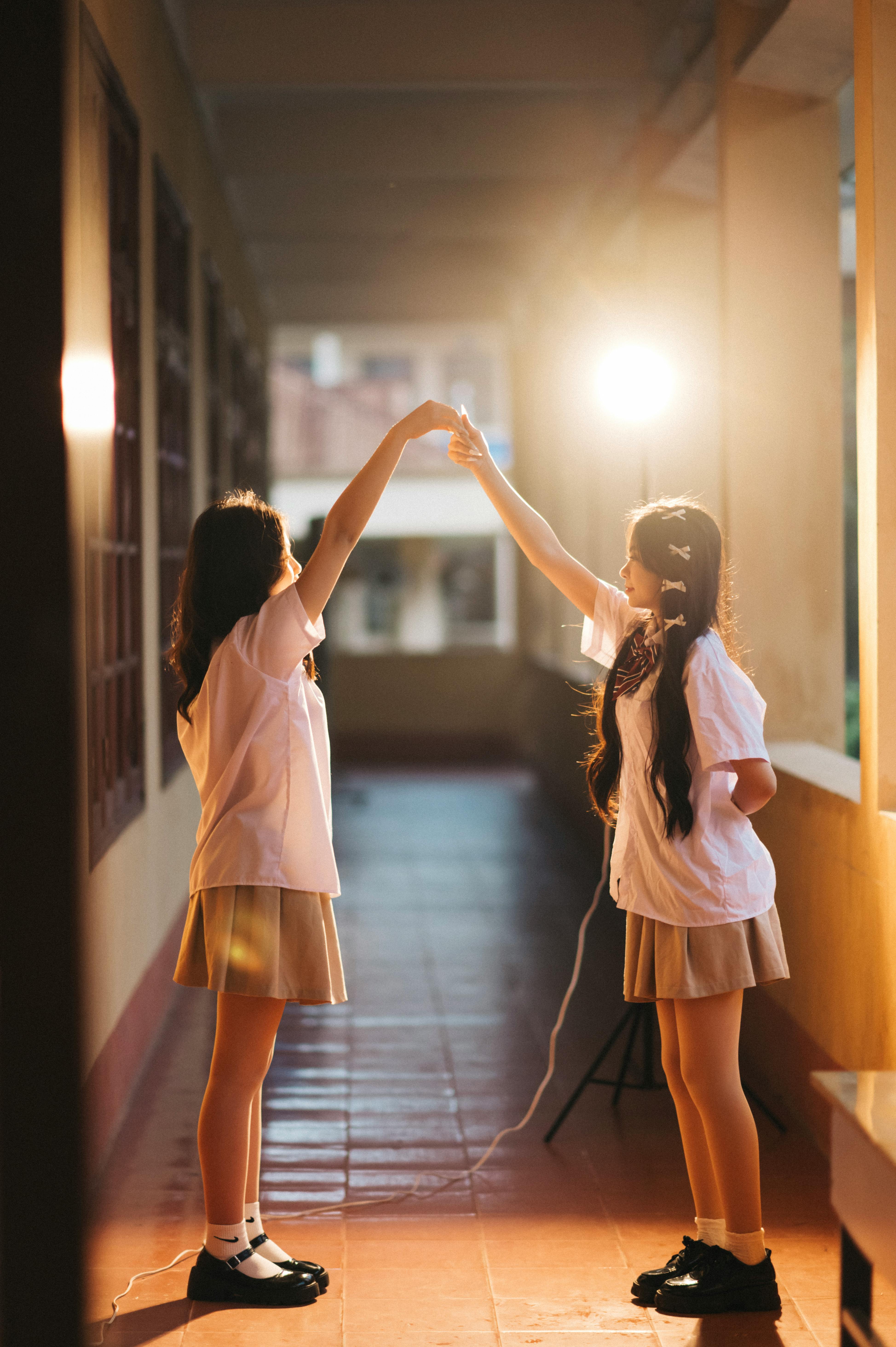 免費 兩名身著校服的女學生在陽光明媚的走廊上跳舞，捕捉了快樂的時刻。 圖庫相片