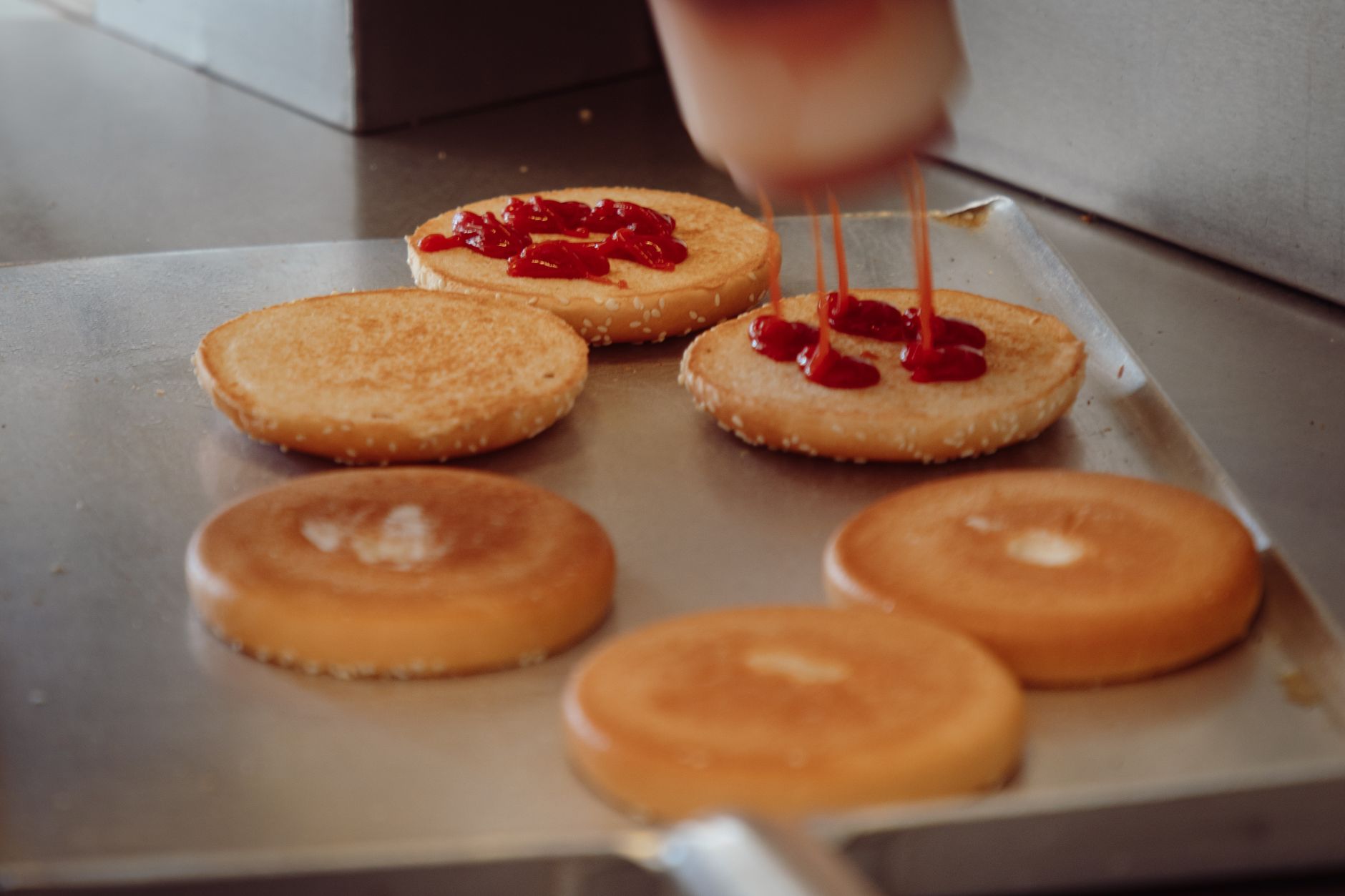 A detailed view of burger buns being prepared with ketchup in a fast food setting.