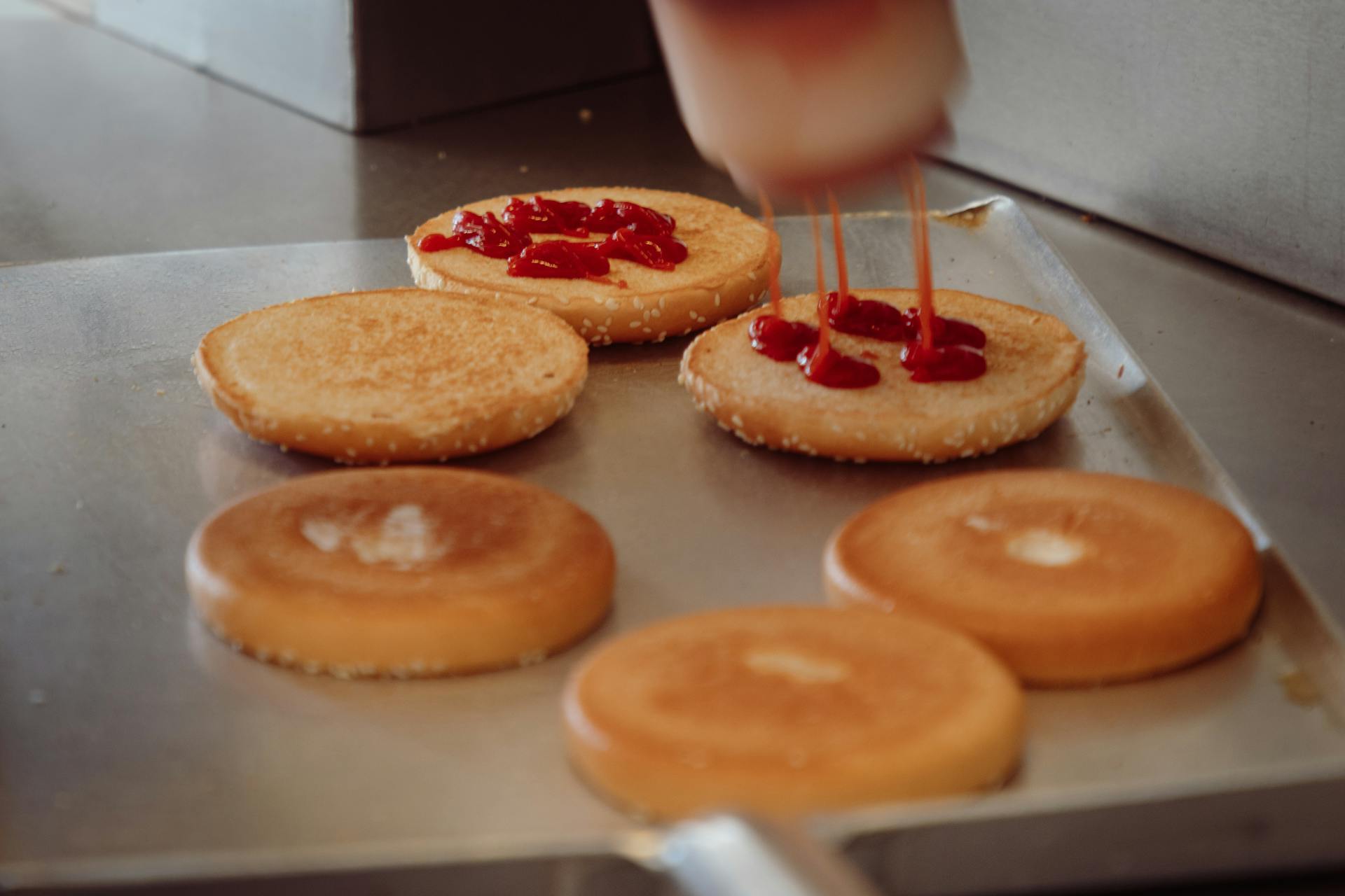 A detailed view of burger buns being prepared with ketchup in a fast food setting.