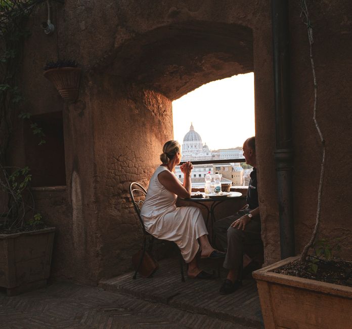 Couple enjoying a romantic dinner with a view of St. Peter's Dome in Rome at sunset.